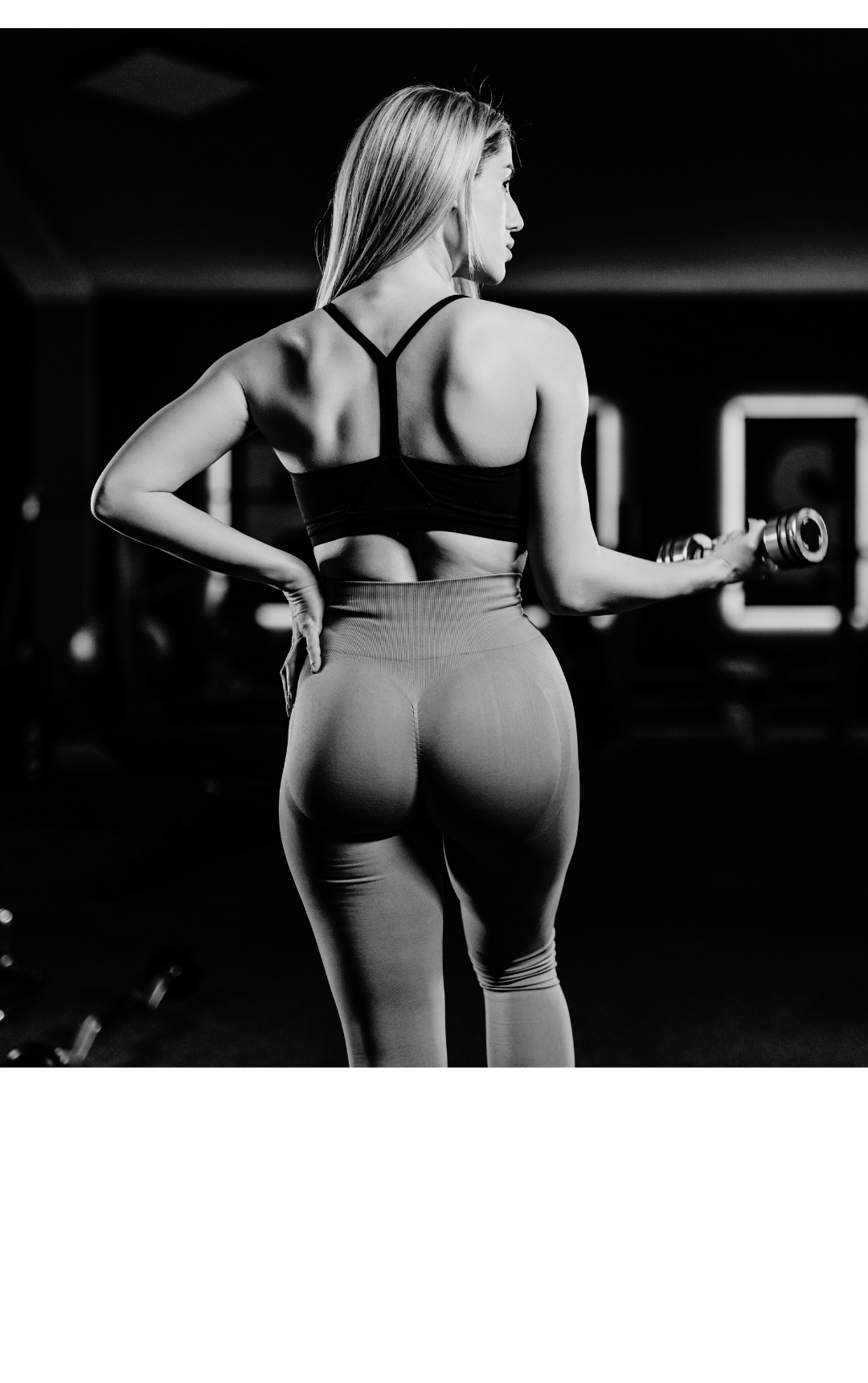 Black and white photo of a woman in workout attire holding a dumbbell in a gym.