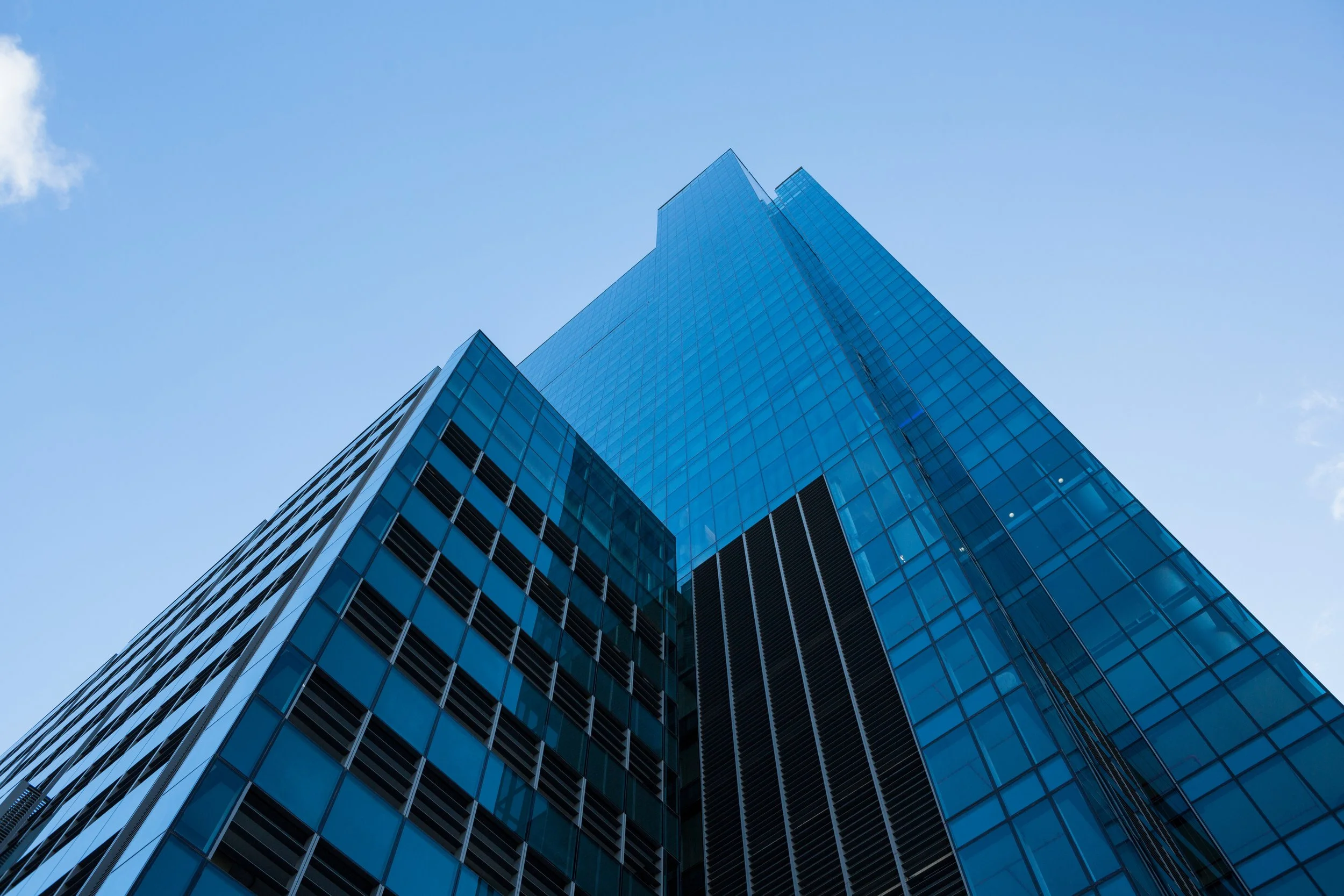A tall glass skyscraper with reflecting glass windows, reaching up toward a blue sky with a few clouds.