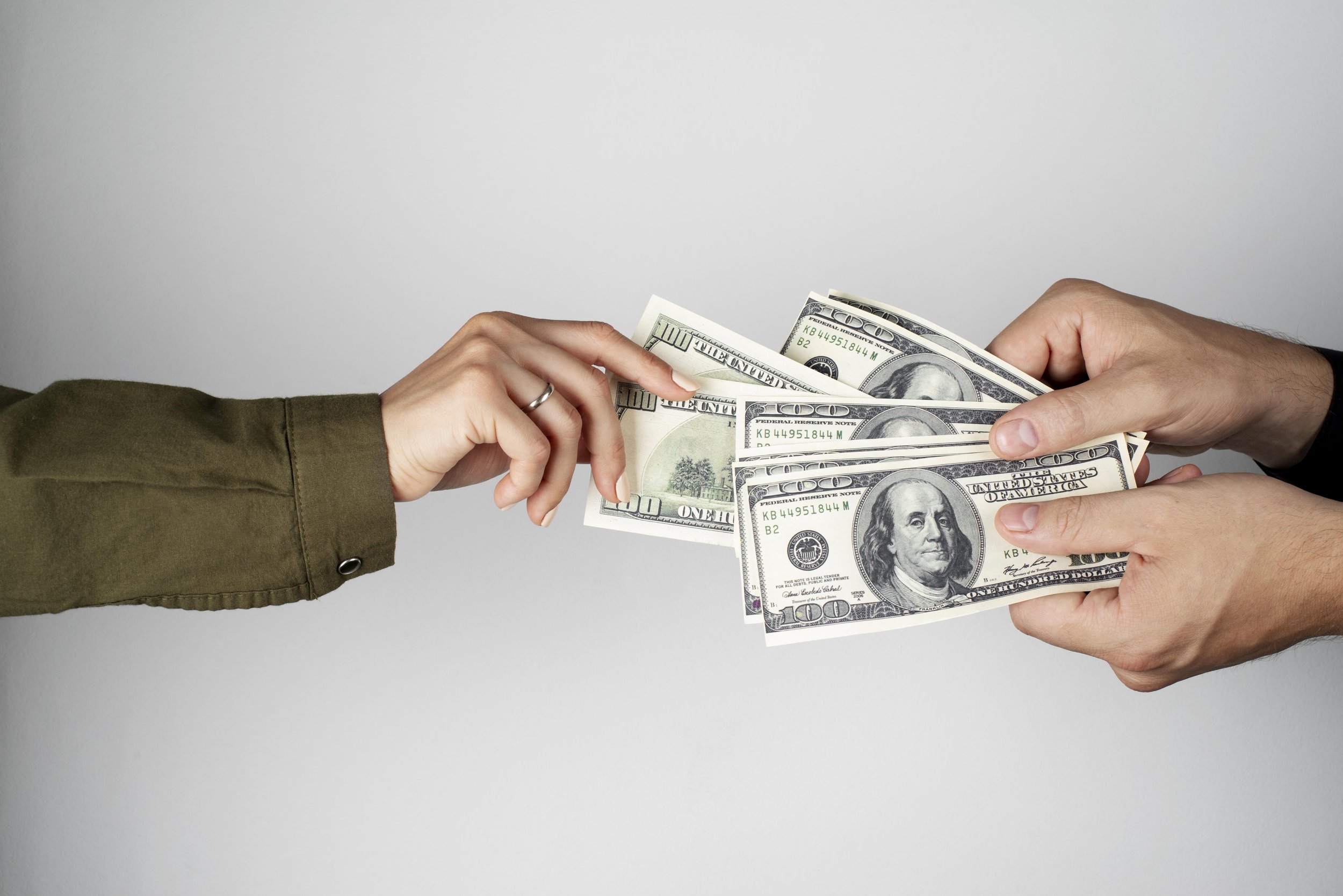 Two people exchanging US$100 bills, one person handing over the money and the other receiving it.