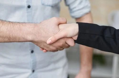 Close-up of two people shaking hands, one in a white shirt and the other in a black jacket.