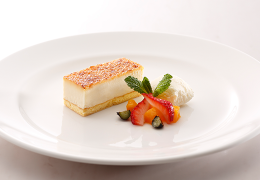 Slice of Japan Saveur Brulee Cheese short cake with strawberries, bananas, and mint leaves on a white plate