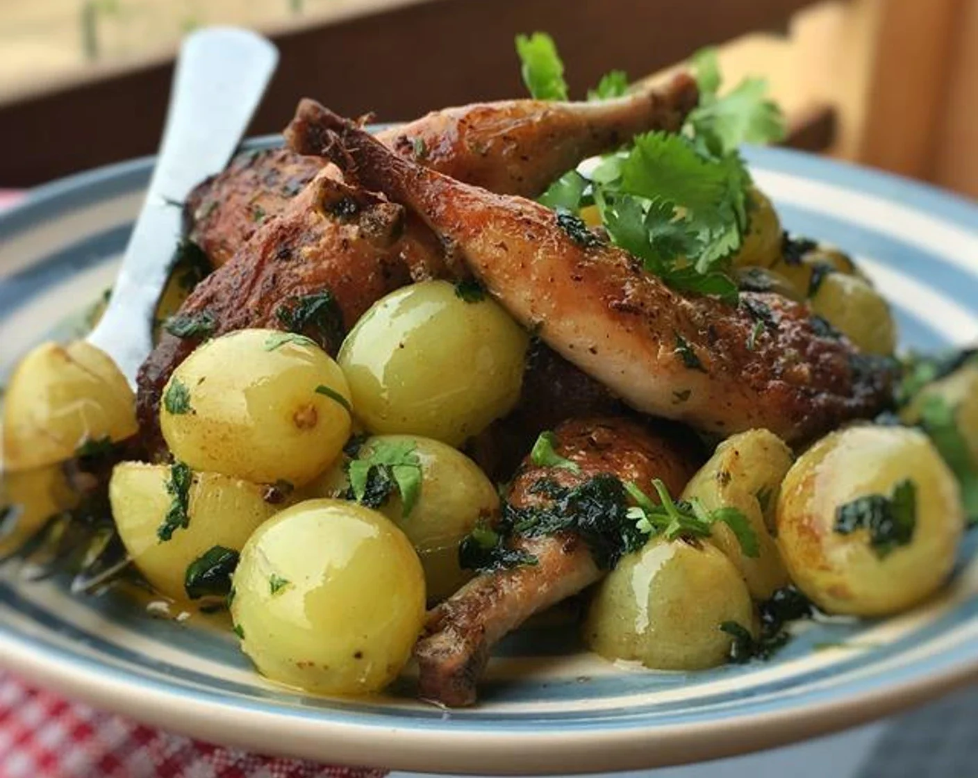 A plate with roasted baby potatoes garnished with herbs and chopped parsley, topped with roasted French Quail Thigh, garnished with fresh cilantro.
