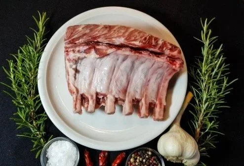 Cesar Nieto Pork Collar (Short Neck) Sliced on a white plate, garnished with rosemary sprigs, garlic, and various spices on a black background.