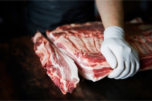 A person wearing a white glove handling a large piece of Cesar Nieto Iberico Pork Japanese Belly Cut (skin off) on a dark surface.