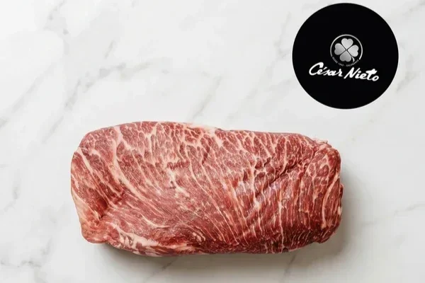 Cesar Nieto Iberico Pork Presa on a white marble surface, with a black circular logo that says 'César Nieto' in the top right corner.