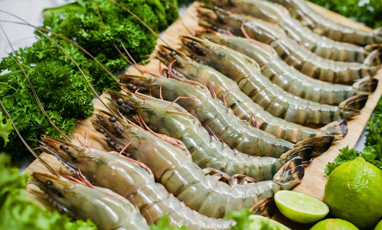 Vietnam Tiger Prawn /Raw shrimp on a wooden platter with lime wedges and green garnishes.
