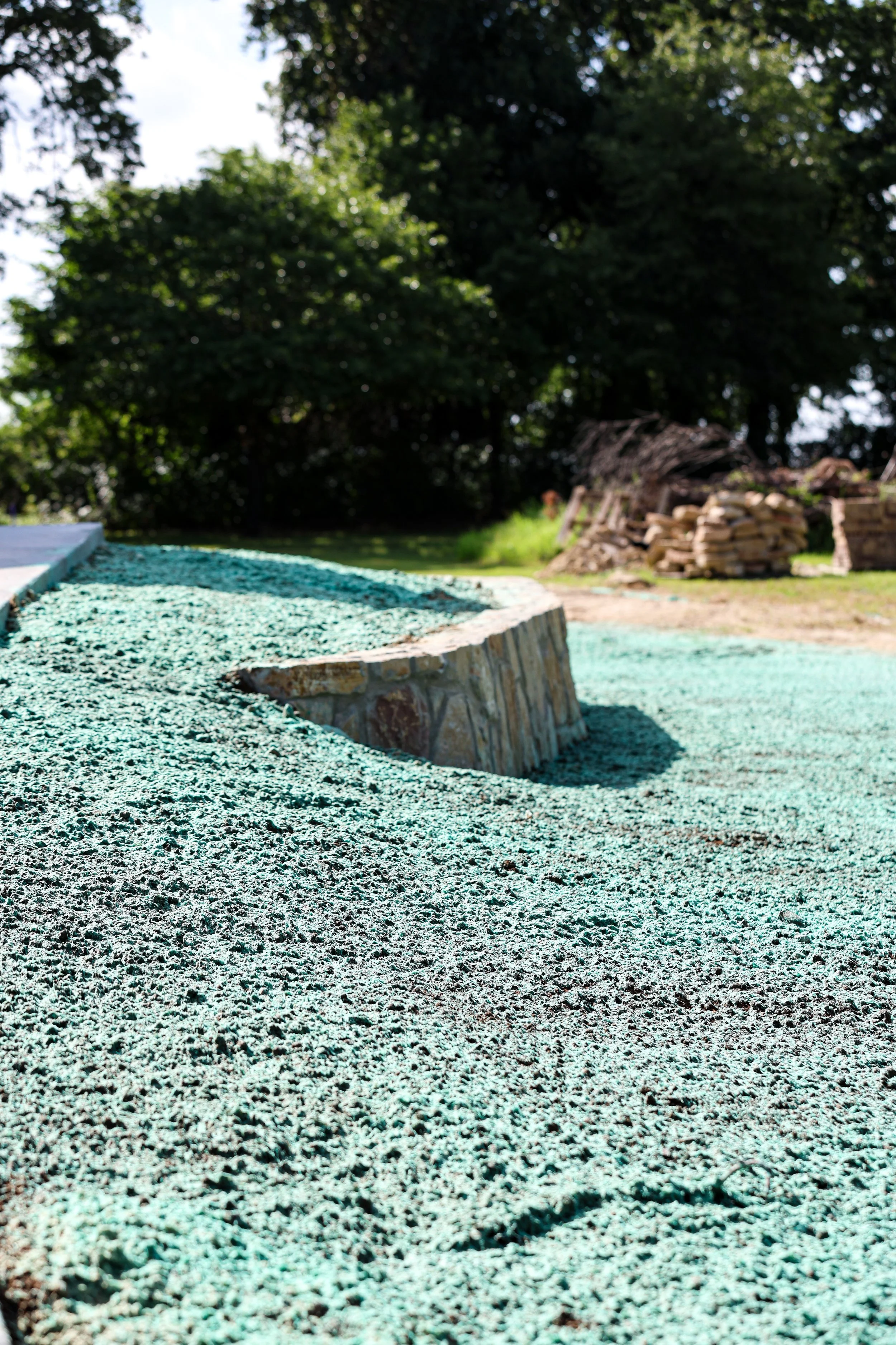 Close-up of a textured, multicolored surface, with a background of trees and a pile of wood logs.