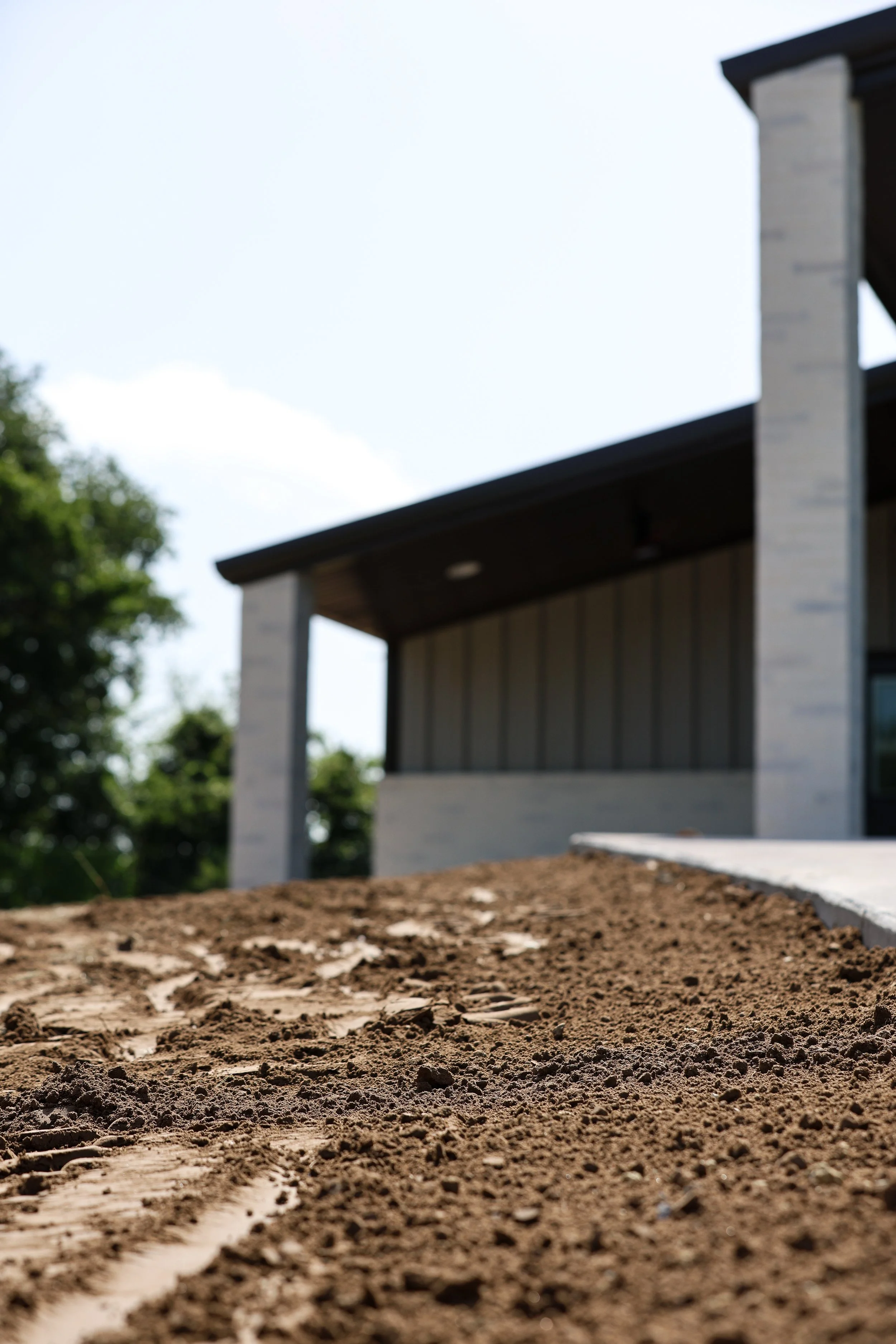 Close-up of a dirt pathway leading to a house with a porch, wooden siding, and a chimney, surrounded by trees.