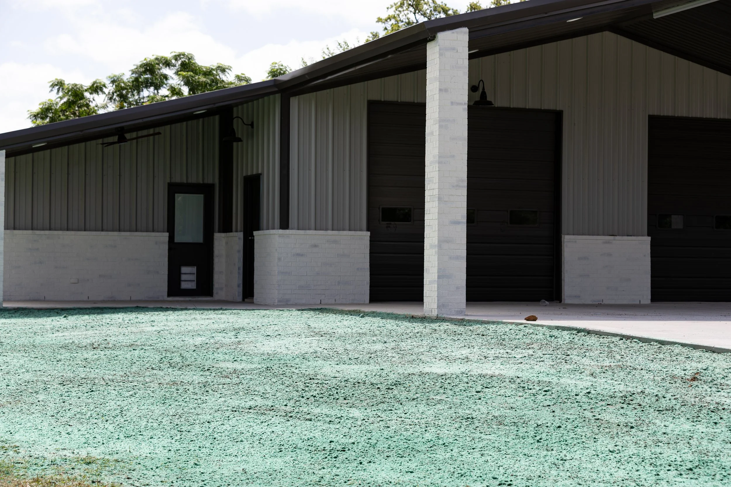 Modern building with metal siding, white brick accents, and a sloped roof, surrounded by greenery and a gravel surface.