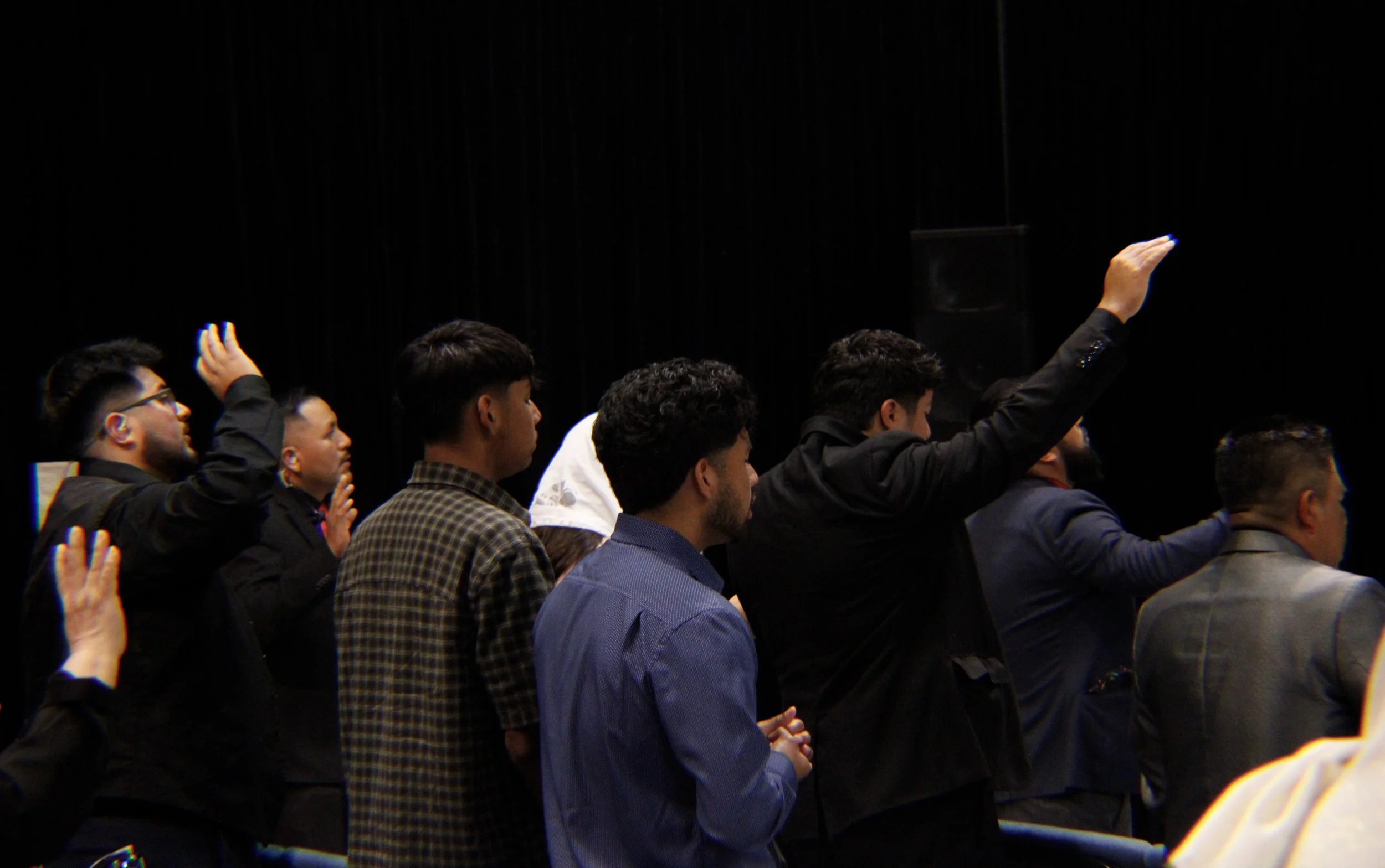 A group of people sitting in a row during an event, some raising their hands to ask questions or participate.