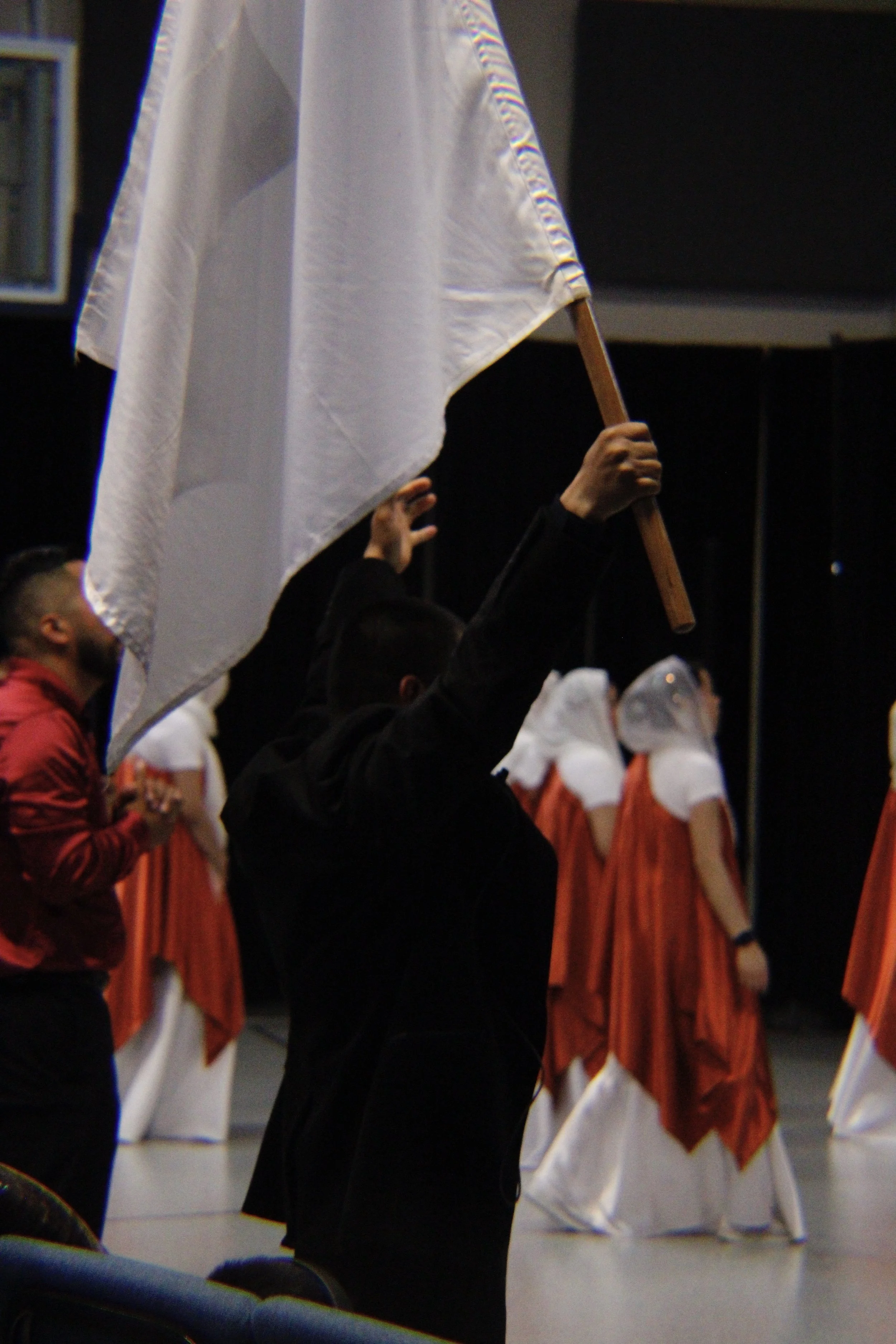 People dressed in choir robes during a performance or rehearsal, with some holding flags and a row of choir members in orange robes in background.
