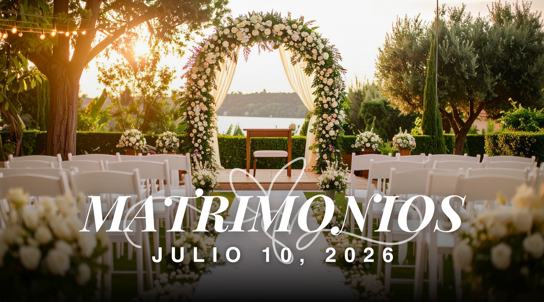 Outdoor wedding ceremony setup with white chairs arranged in rows, floral arch with white flowers and greenery, and a scenic water view in the background during sunset.