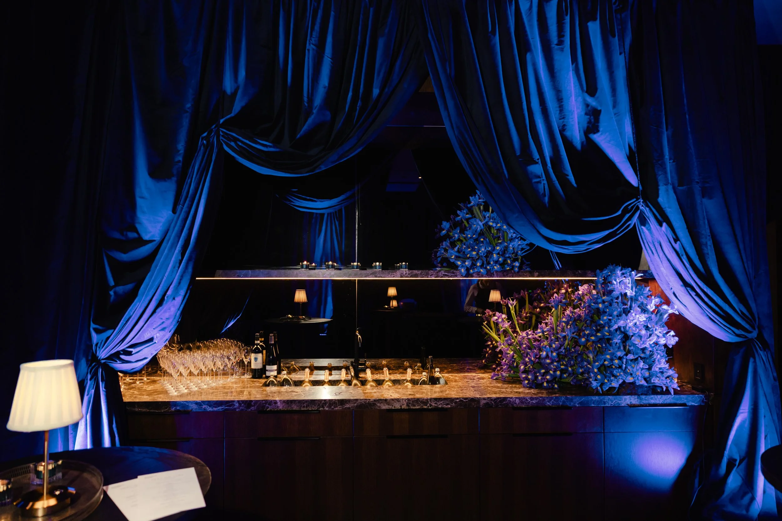 Stage with blue curtains, floral arrangements, and a bar setup.
