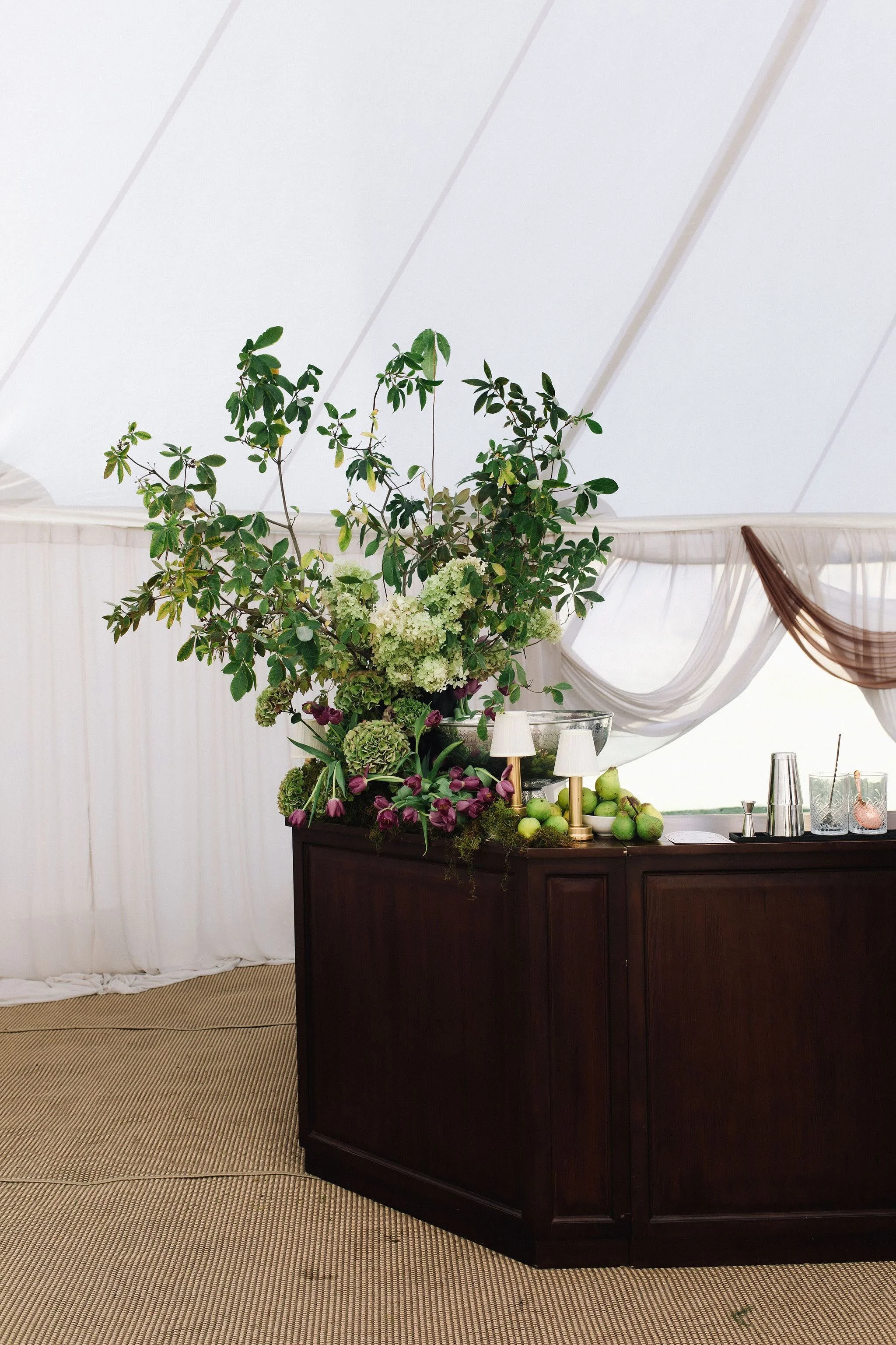 A floral arrangement on a dark wooden sideboard with white drapery and a white ceiling in the background.