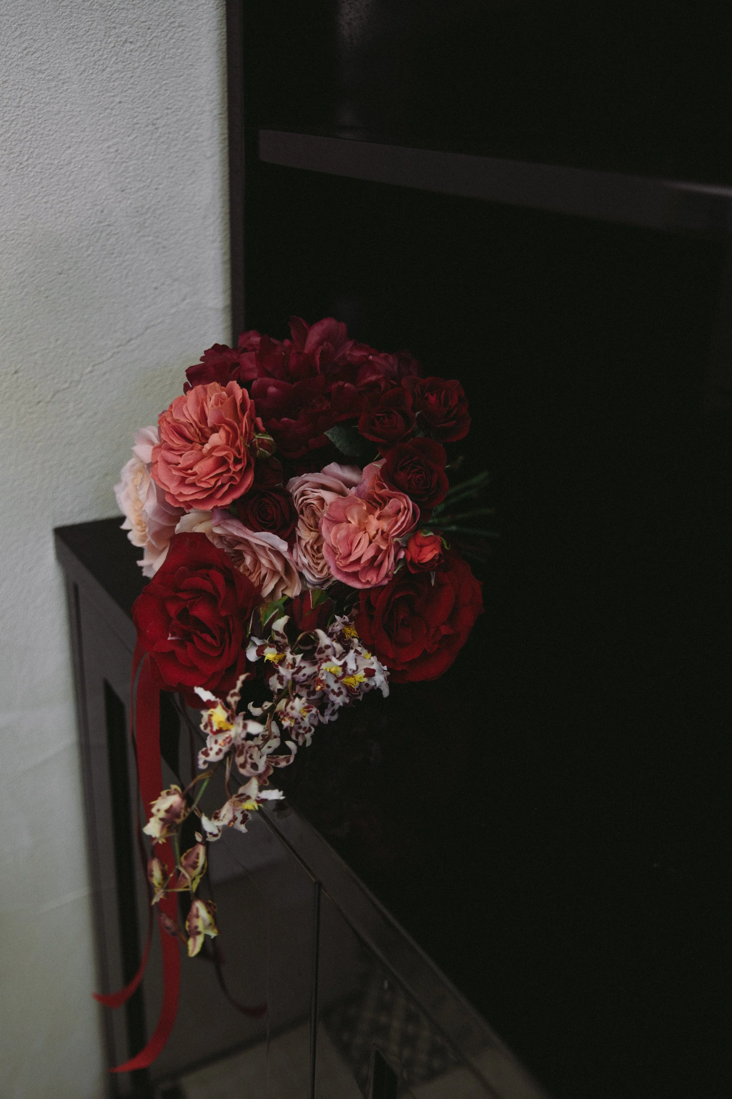 A bouquet of red, pink, and white artificial flowers resting on a black piece of furniture.