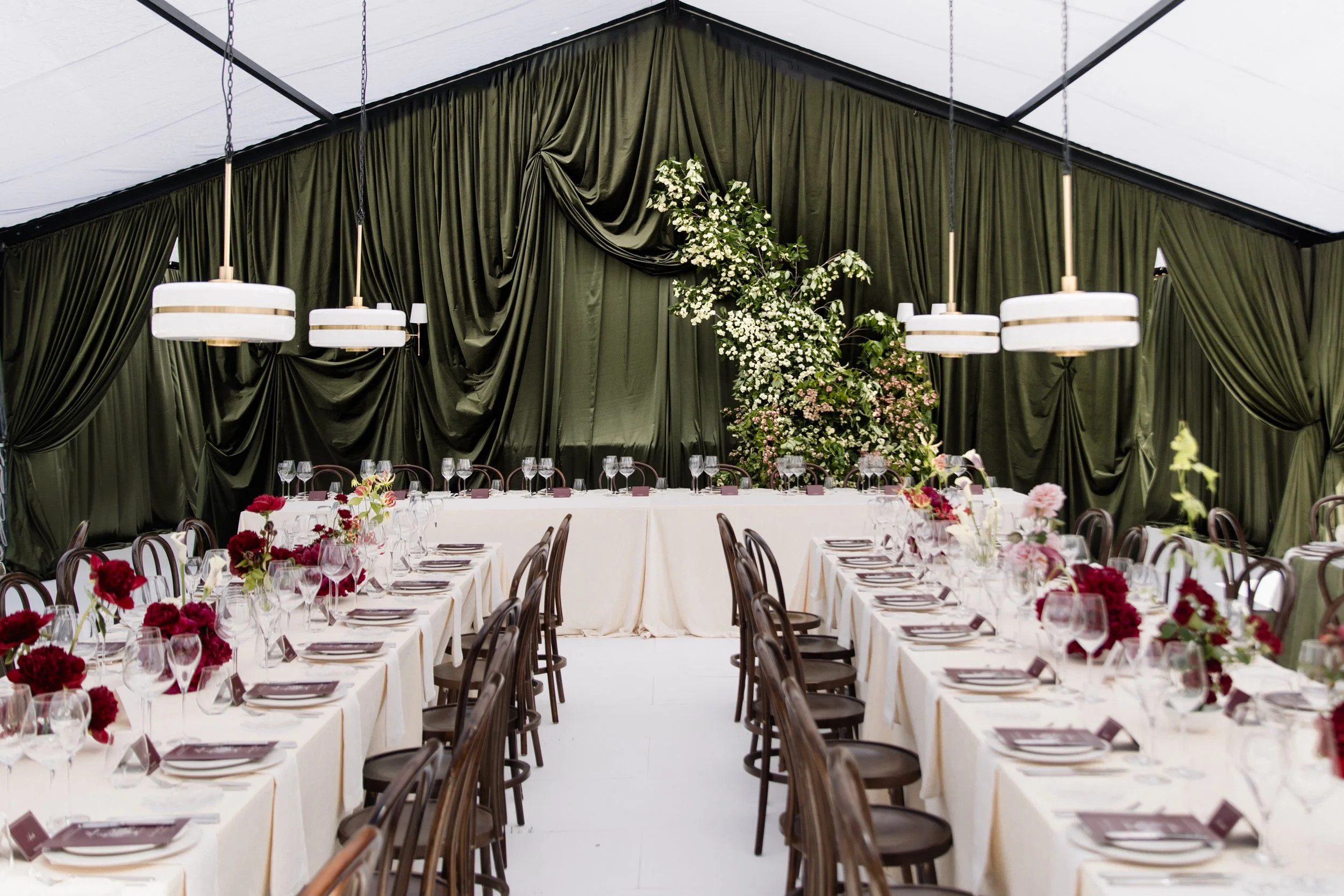 Elegant event hall with draped dark green curtains, large floral arrangements, and round tables set for a formal occasion.
