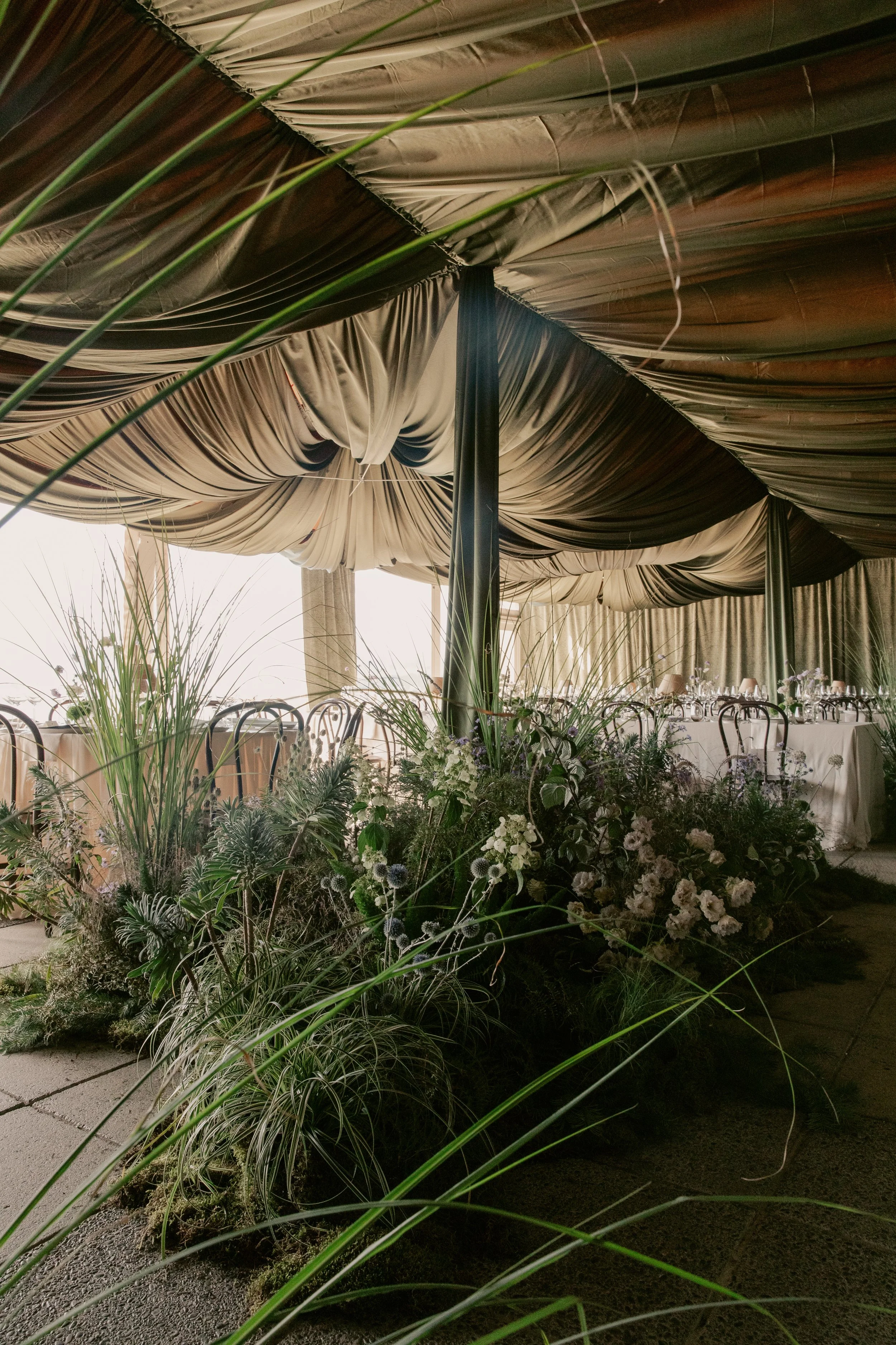 Indoor event space with draped ceiling fabric, floral arrangements, and tables set for a gathering.