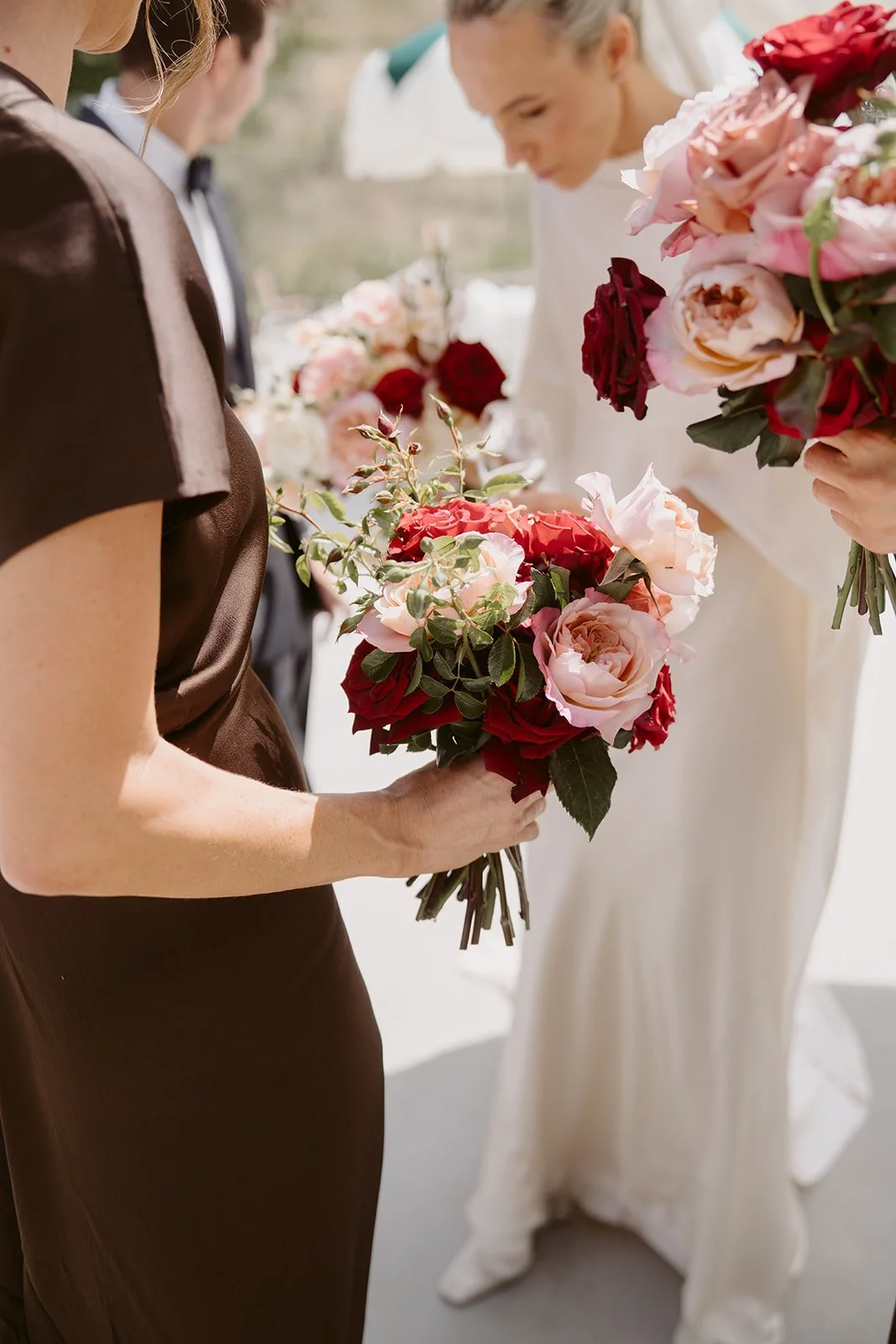 Three women holding bouquets of pink, red, and white roses at a wedding or event.