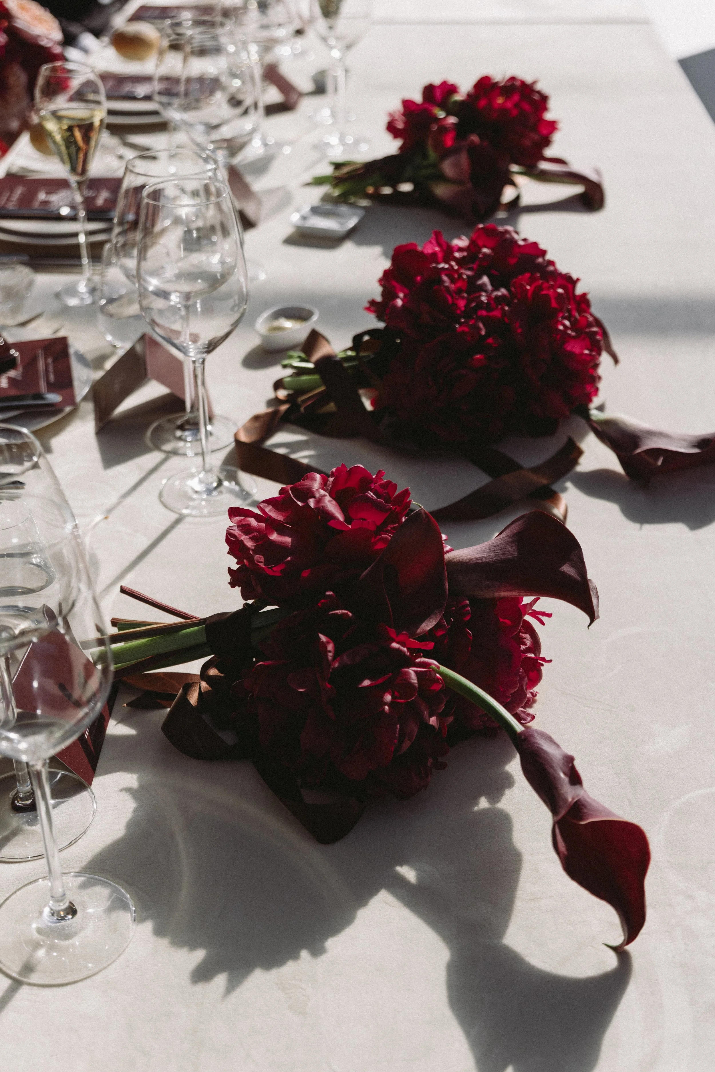 A table decorated with burgundy flowers and multiple wine glasses, set for a special occasion or celebration.