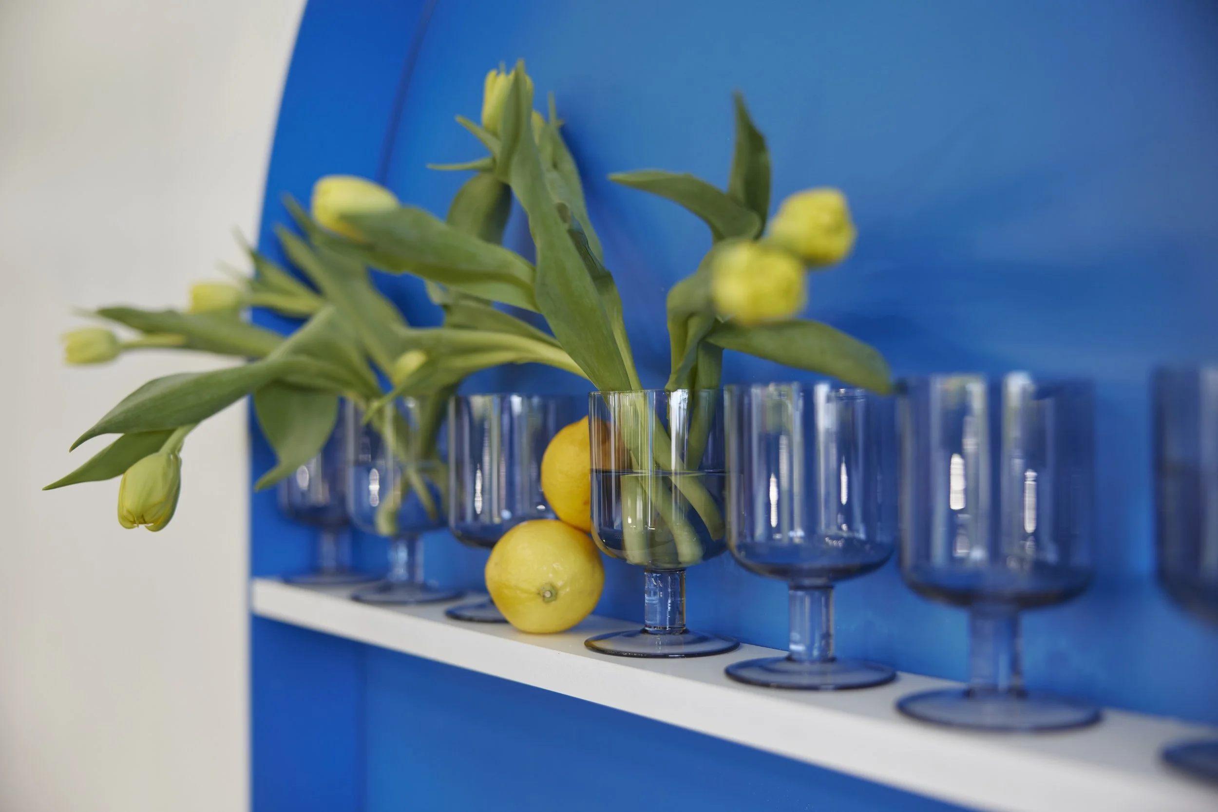 Vase with yellow tulips and lemons, against a blue background.