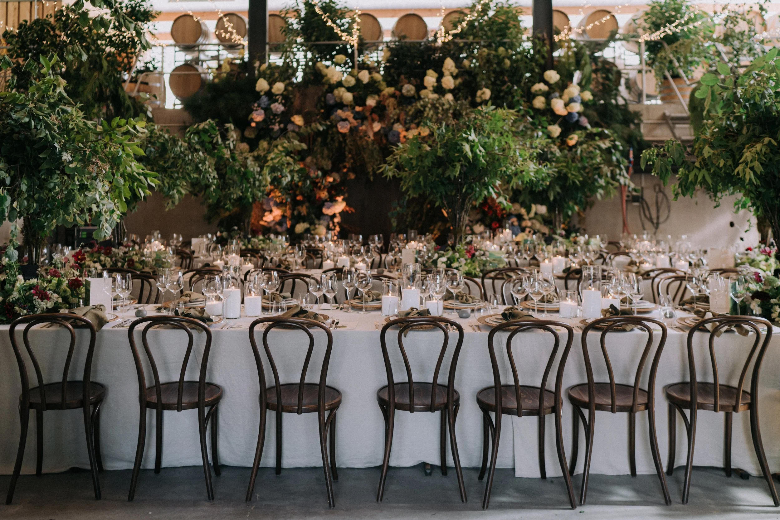 Elegant indoor event space decorated with lush green plants and white flowers, set up with round tables and chairs for a formal occasion.