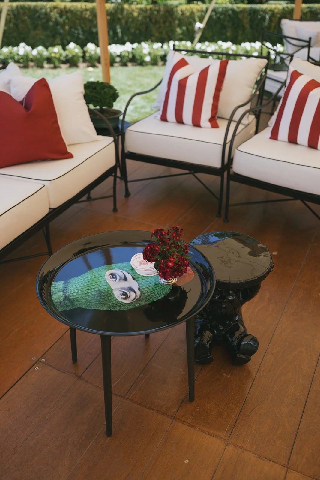 Outdoor patio seating area with white cushioned chairs featuring red and white striped pillows, a black coffee table with a pug print, a smaller side table, and a small bouquet of red flowers