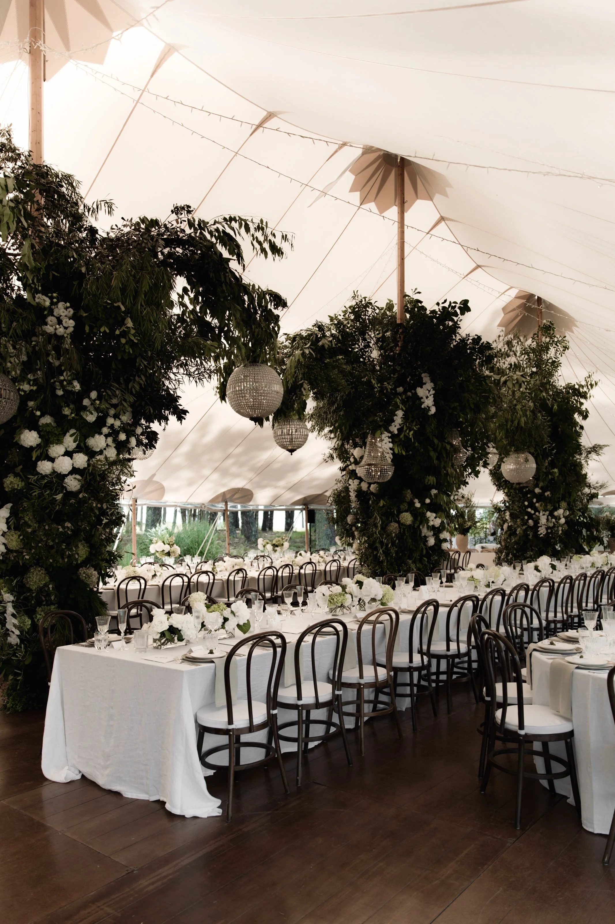 Elegant banquet hall decorated with white flowers, chandeliers, and a white tent ceiling, set up for a formal event.