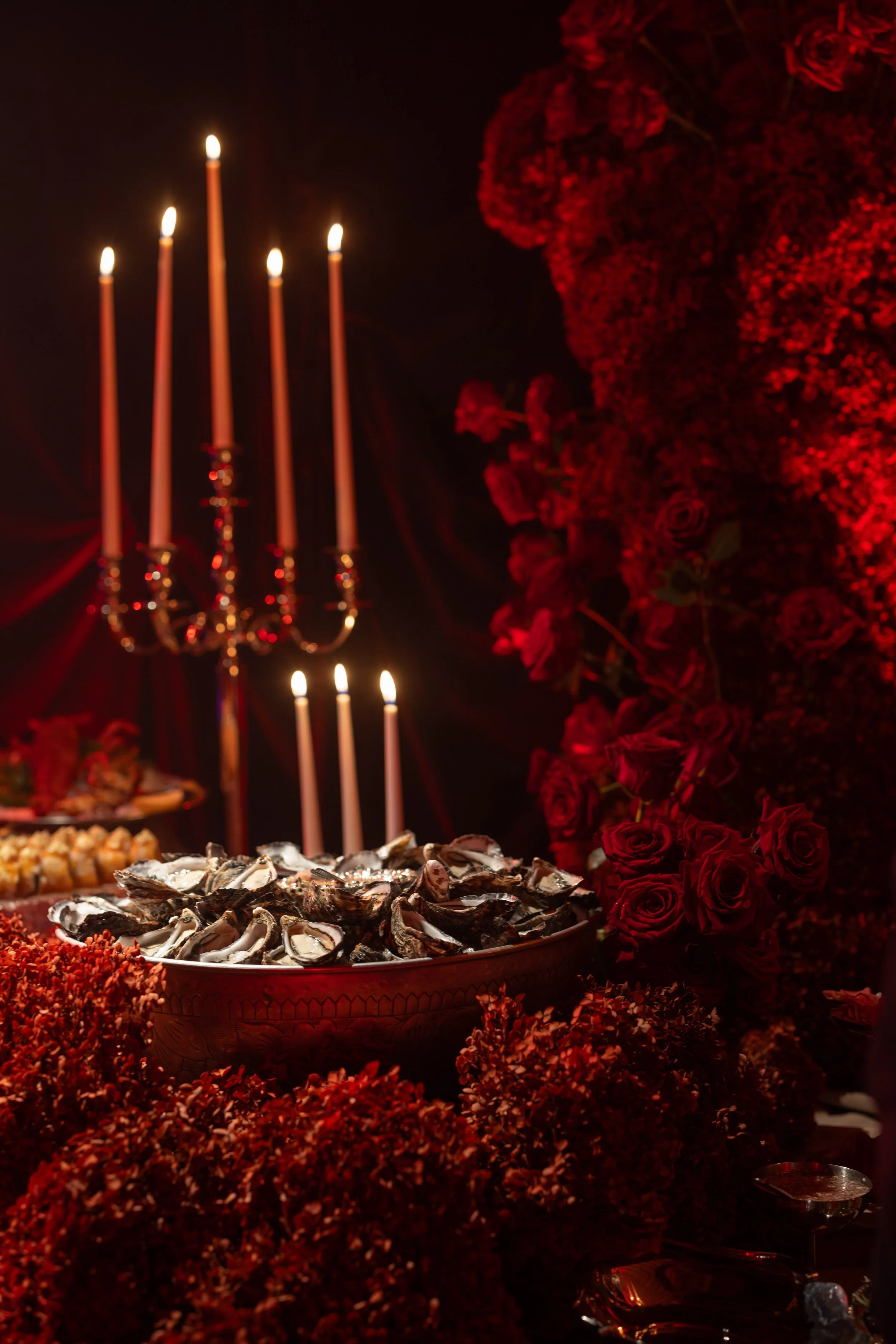 A table set with seafood, surrounded by red flowers and lit candles, at a celebration or dinner event.