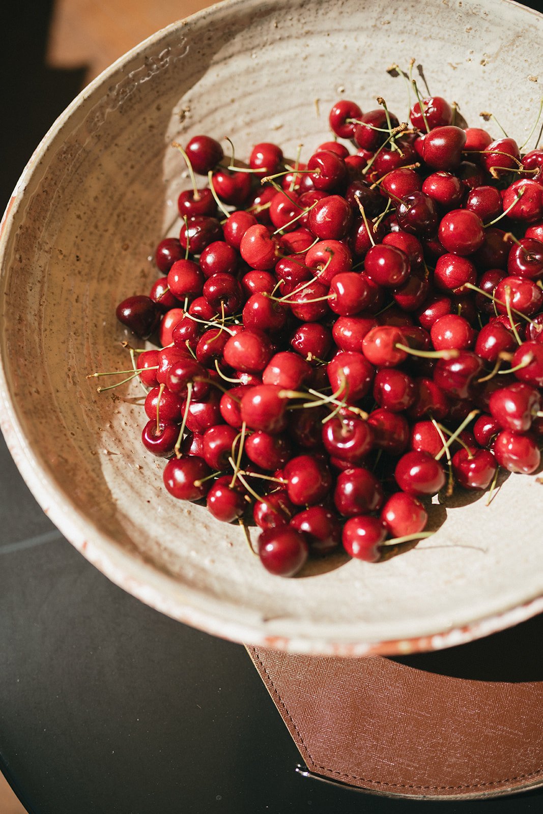 Fresh red cherries in a ceramic bowl on a dark table with a pink napkin.