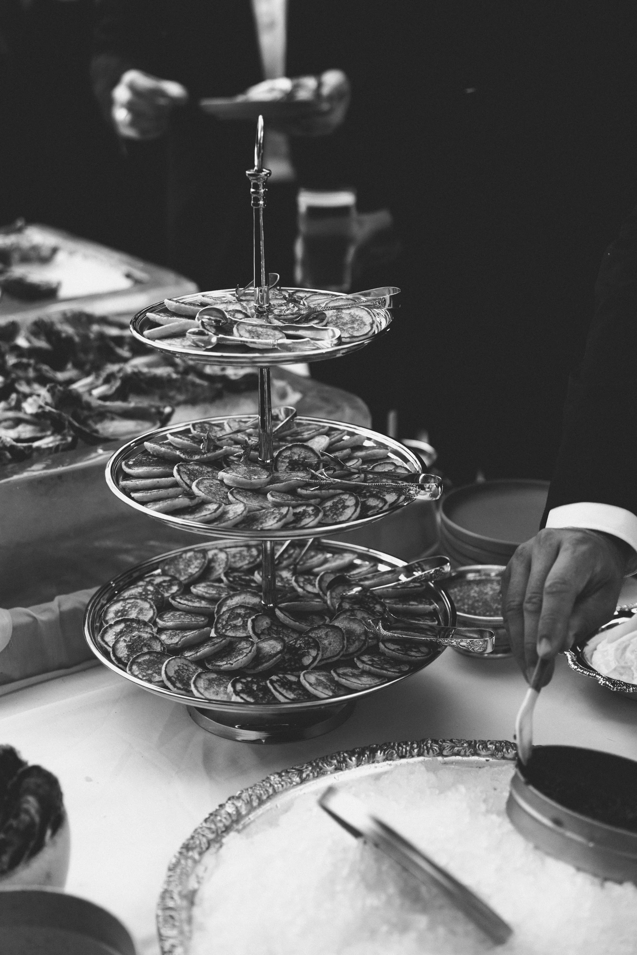 Multiple dessert trays with sliced fruit or cake, with a person serving or preparing desserts in the background.