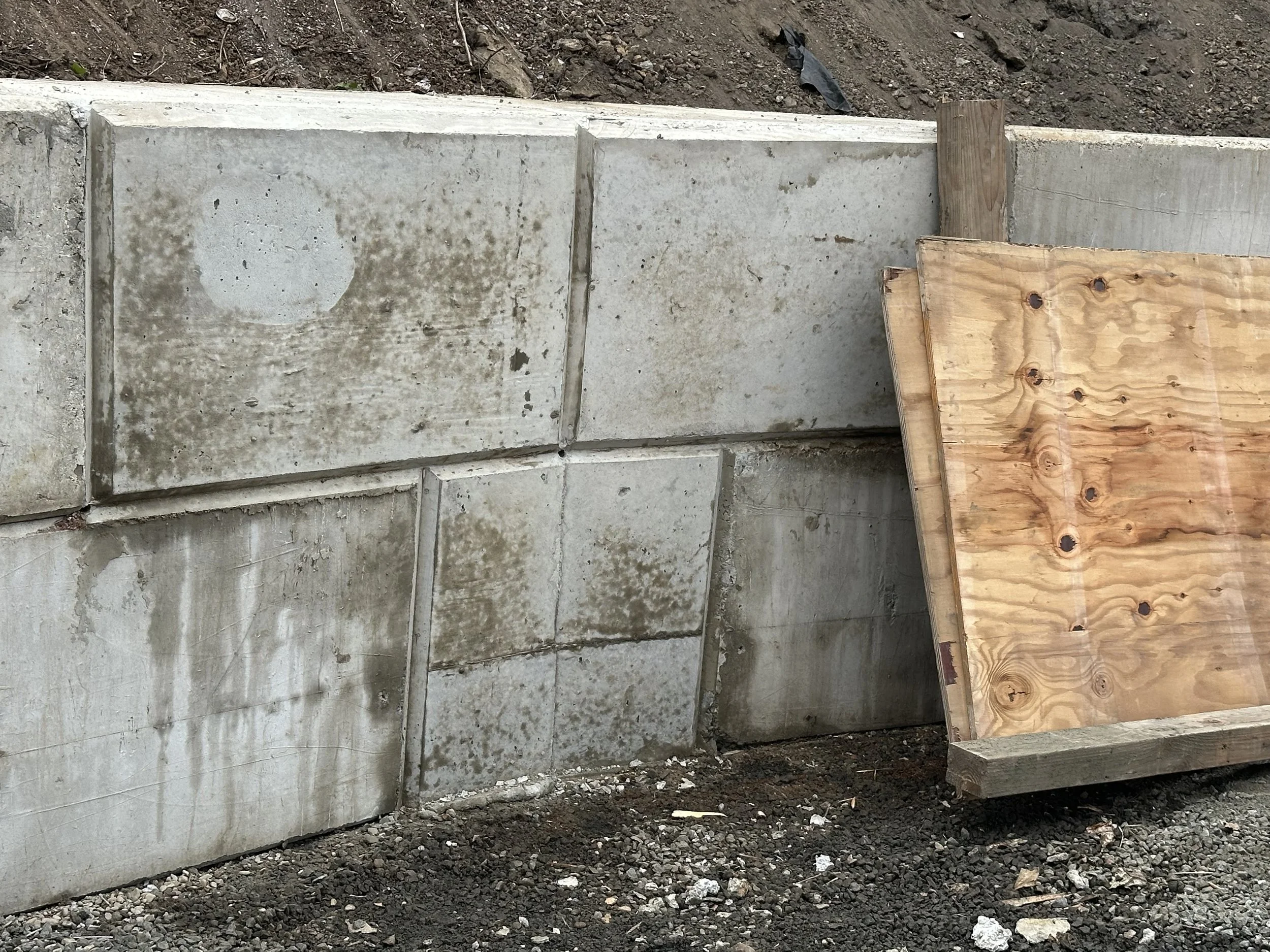 Concrete blocks stacked on ground next to dirt and soil, with a wooden plank resting on top.