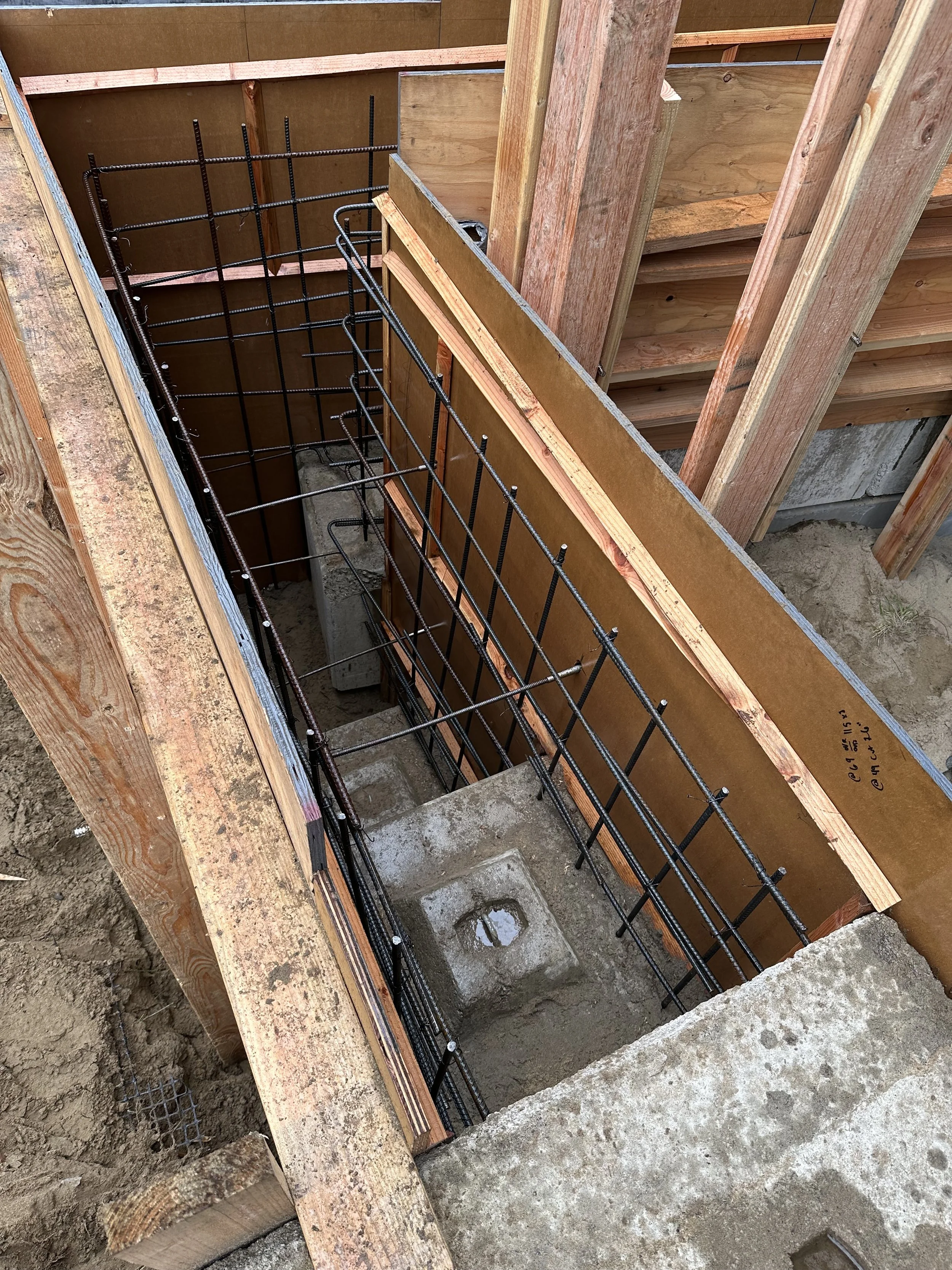 Construction site with wooden framing, steel rebar, and concrete foundation forming a staircase.