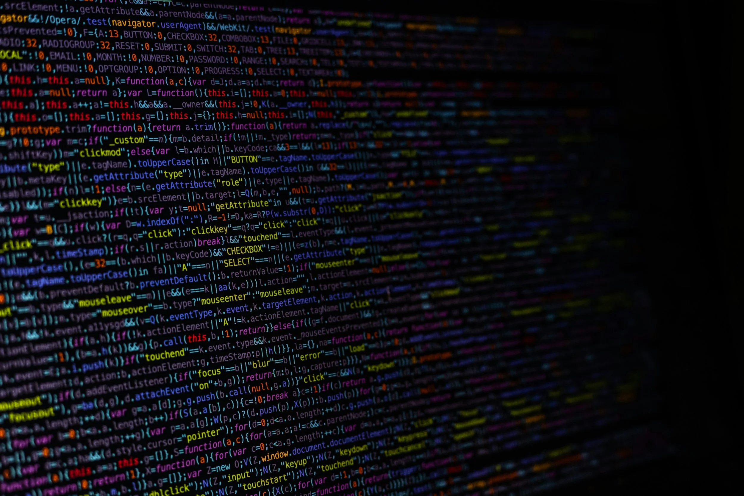 Close-up of a computer screen with colored programming code, including JavaScript and HTML elements, displayed in a dark environment.