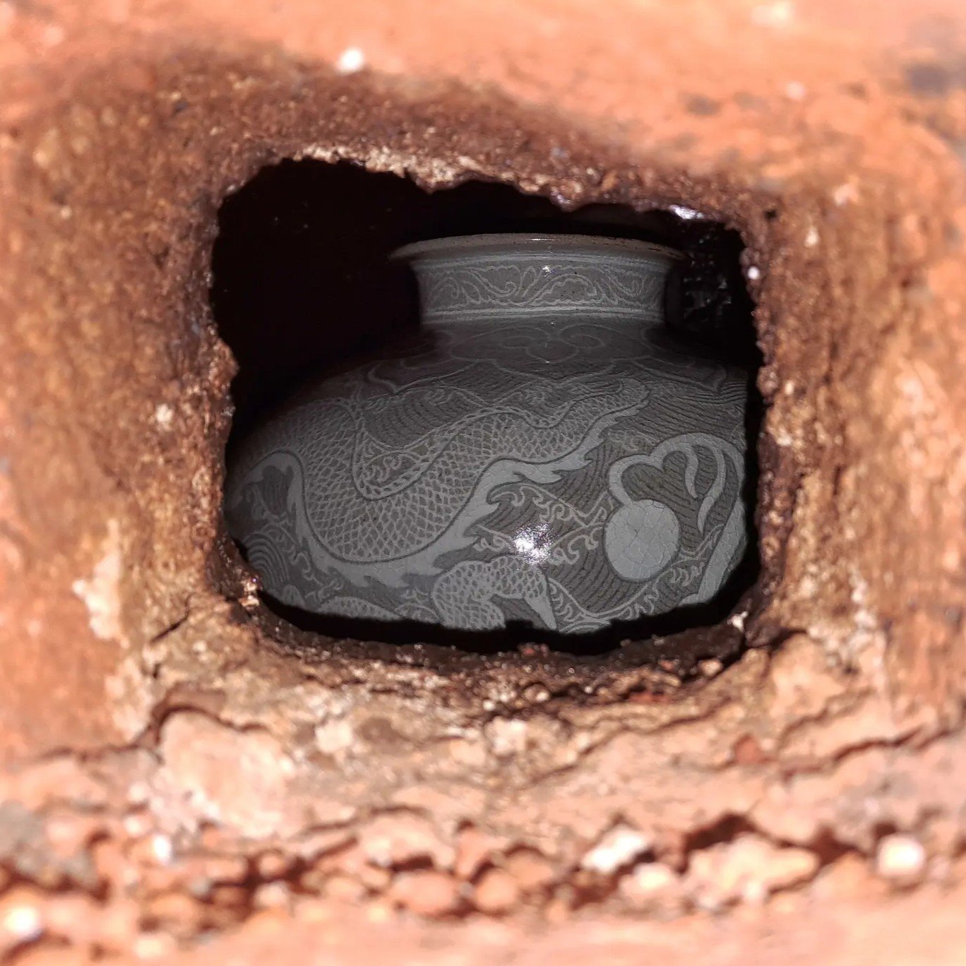Inside a rusty pipe, an engraved ceramic plate with a dragon design is visible.