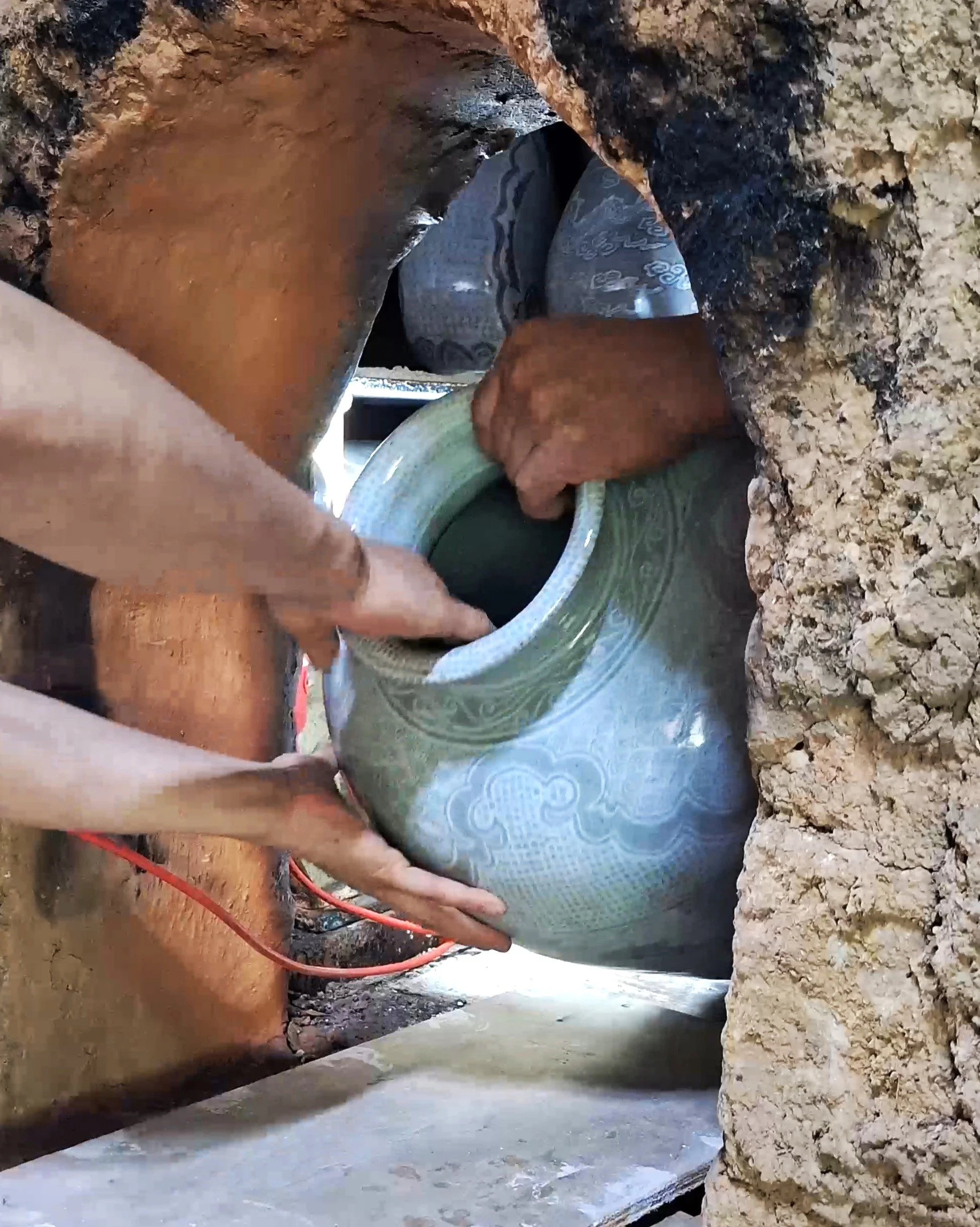 A person working in a narrow underground tunnel, using a flexible pipe, with rough rocky walls surrounding them.
