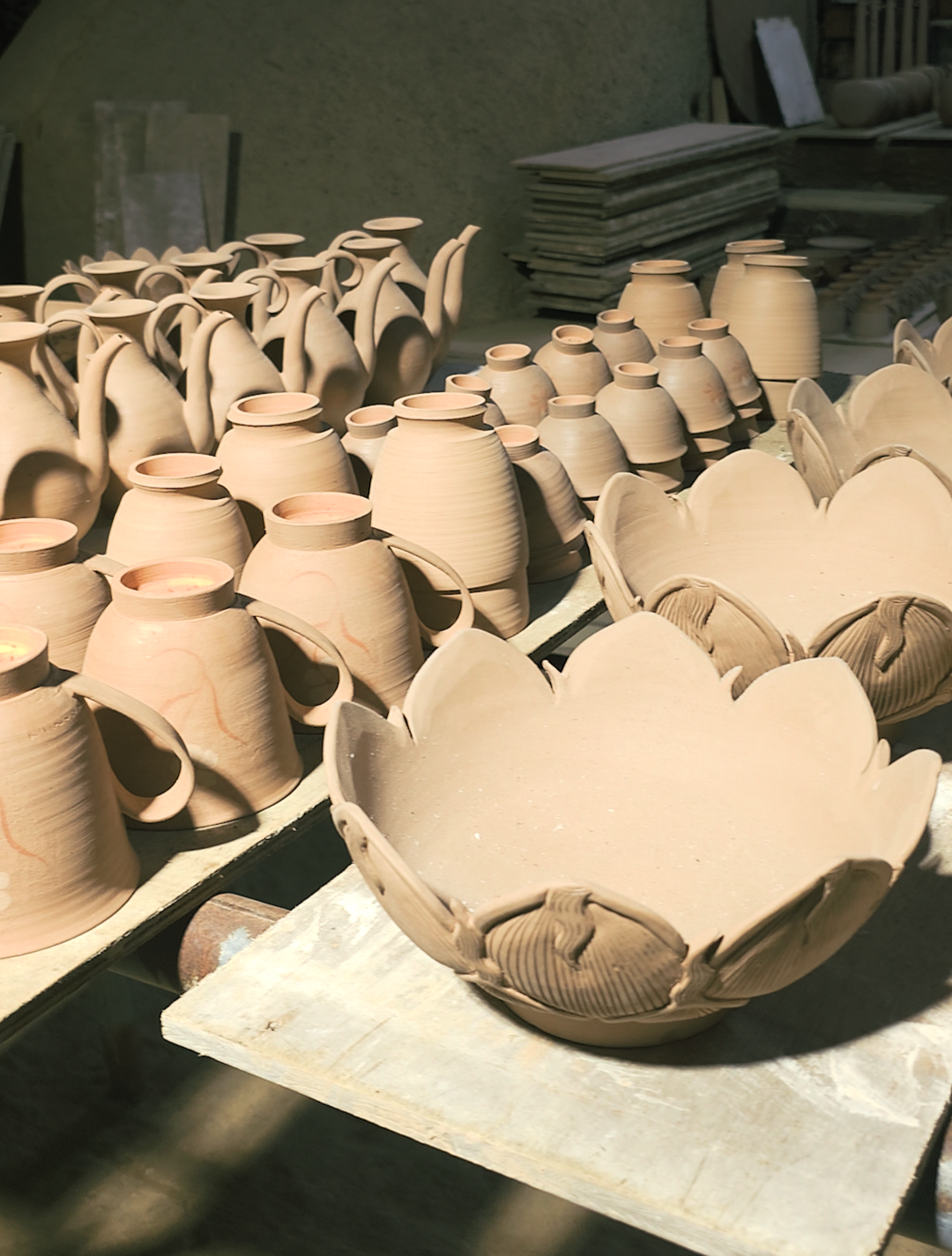 Unfinished pottery pieces, including vases and a decorative bowl, arranged on tables in a ceramics workshop.