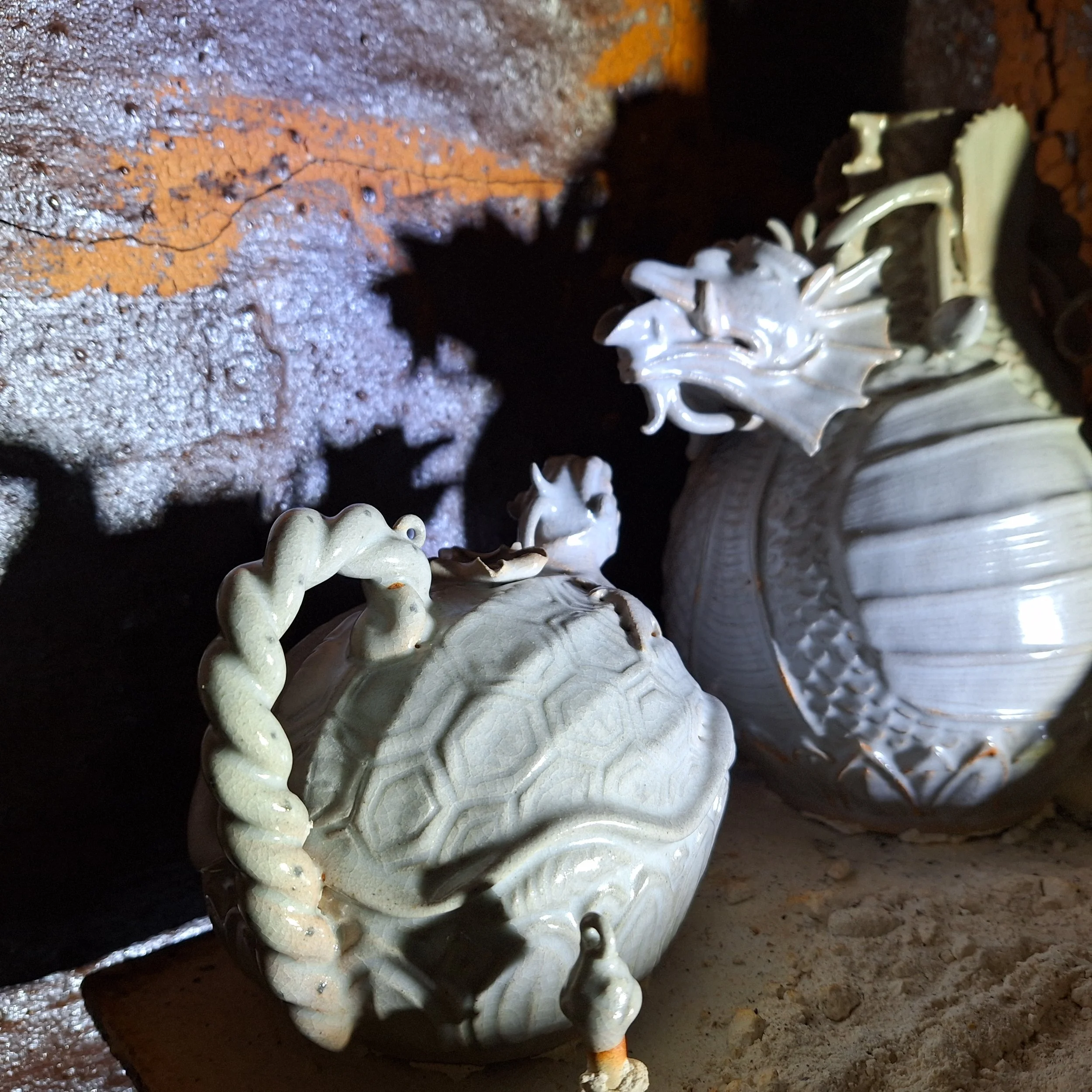 Close-up of white decorative ceramic objects, possibly ornaments or furniture embellishments, on a rough, dark surface with some textured and rusty areas.