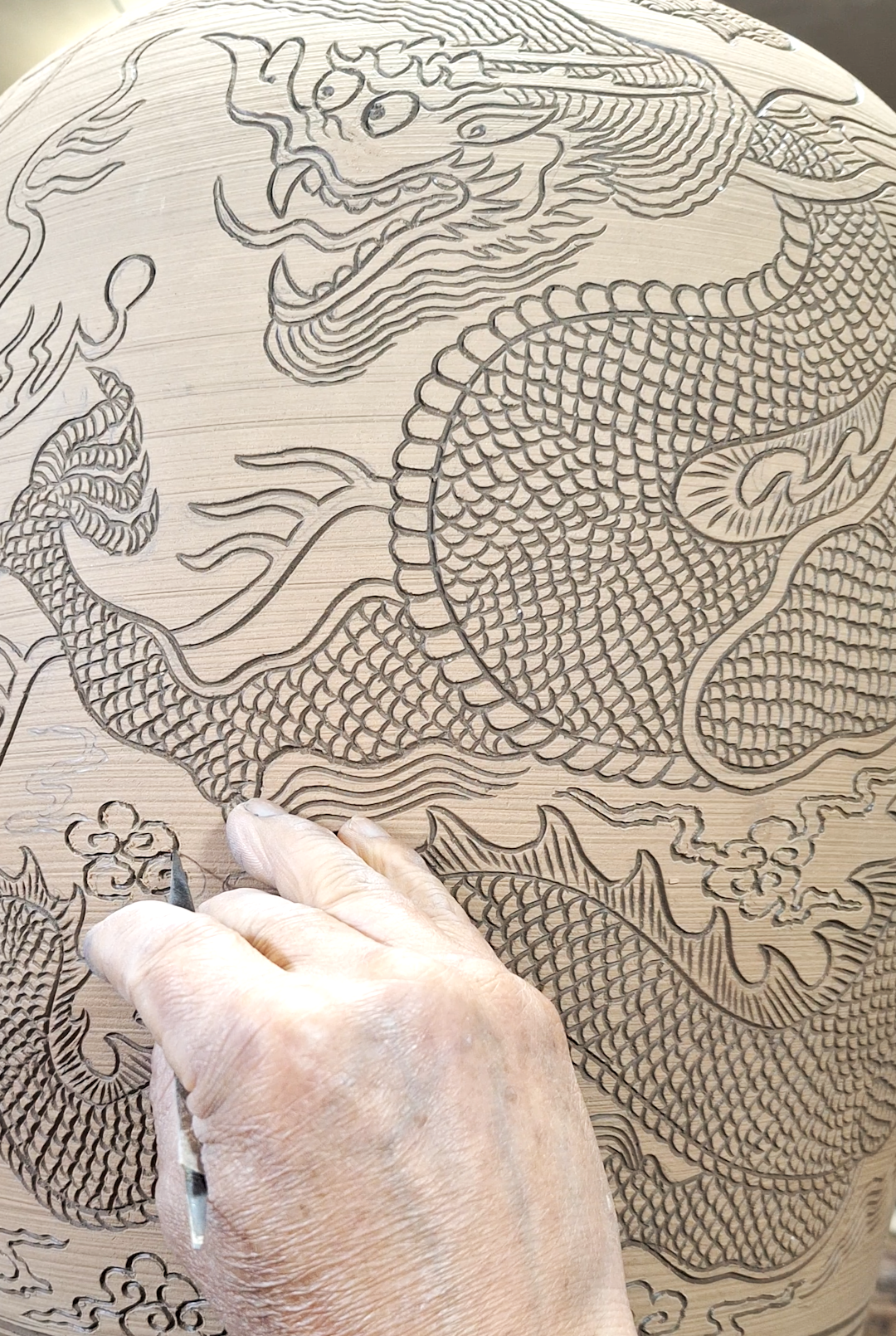 A person carved an intricate dragon design into a round wooden surface.