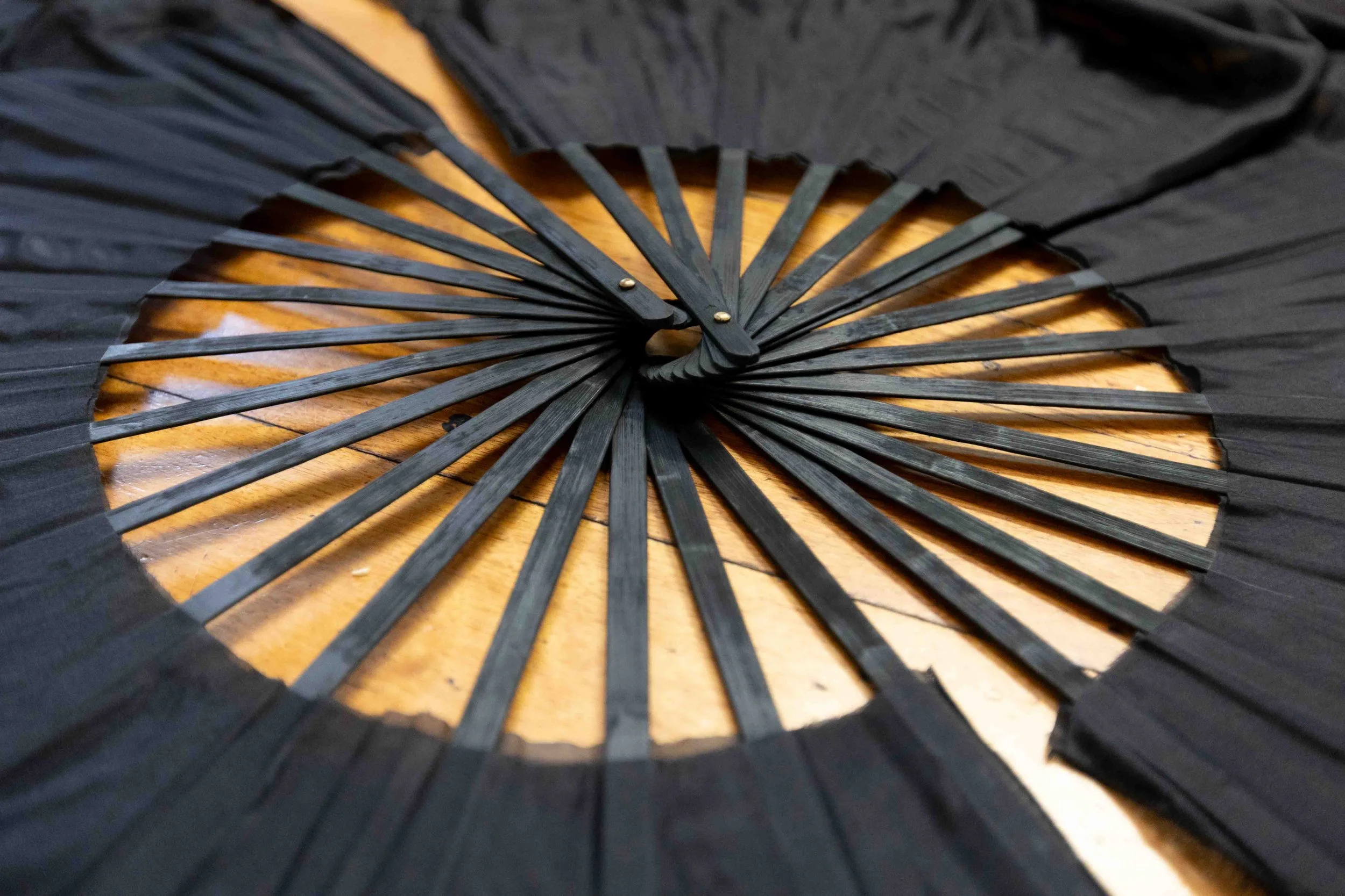 Black folding fan partially opened on a wooden surface.
