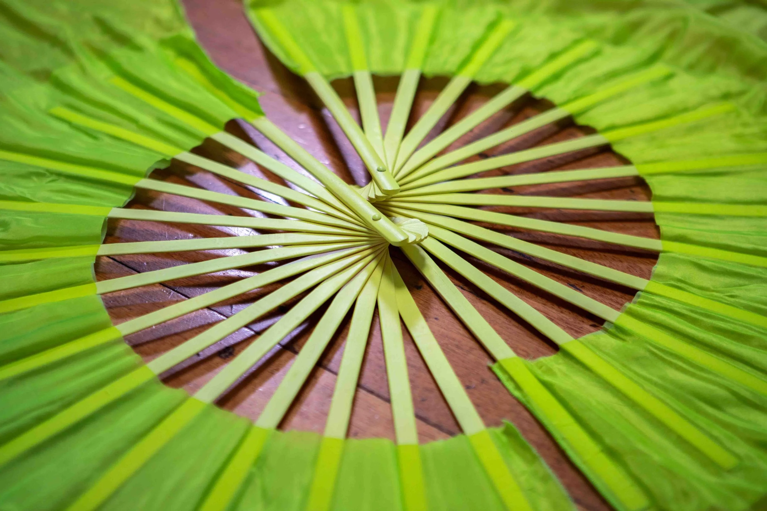 A close-up view of a decorative green paper fan with yellow ribs, placed on a wooden surface.