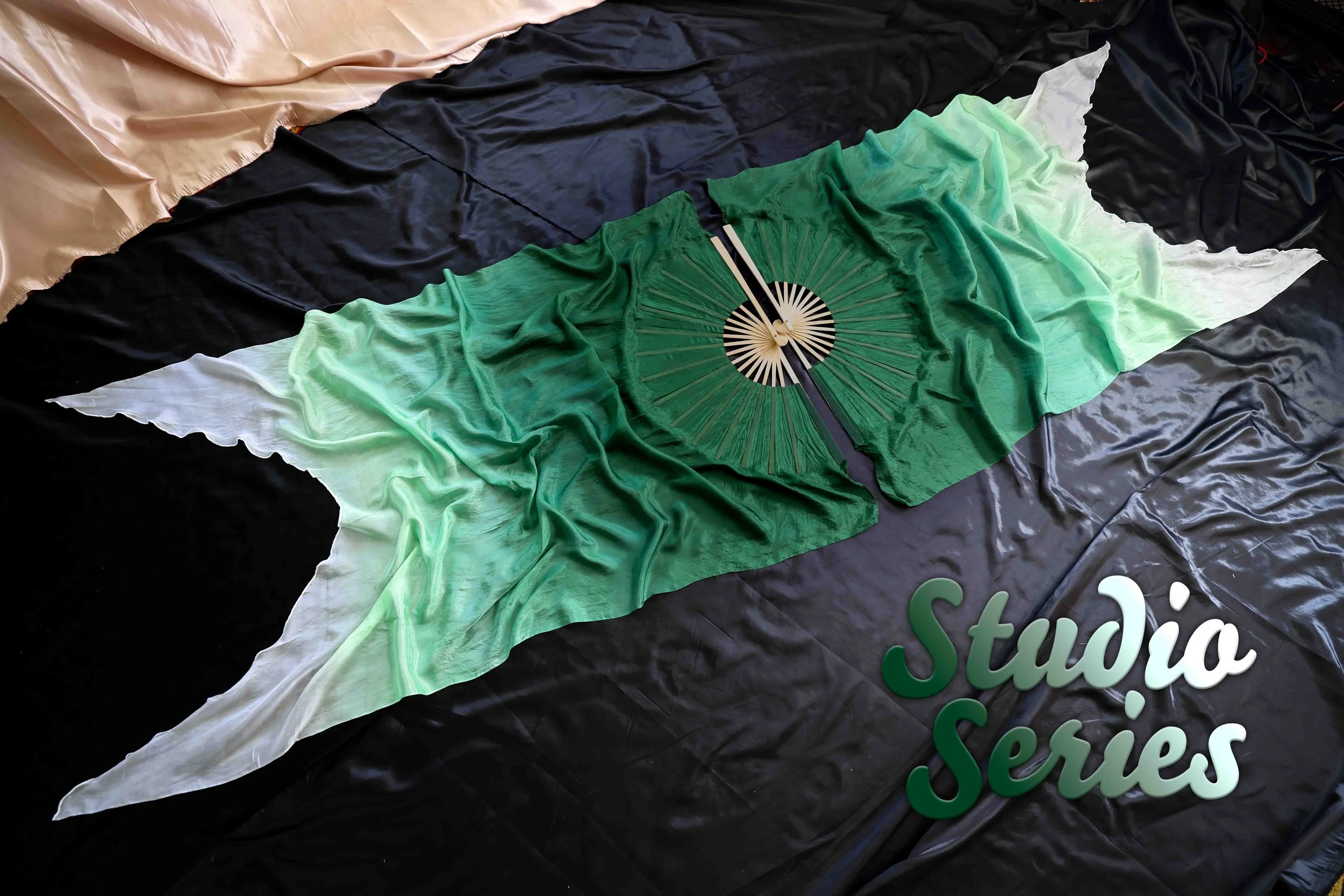Colorful fabric with a black circular paper fan featuring a swan and chopsticks on top of a black cloth with the partially visible words 'Studia...' in white and green text.