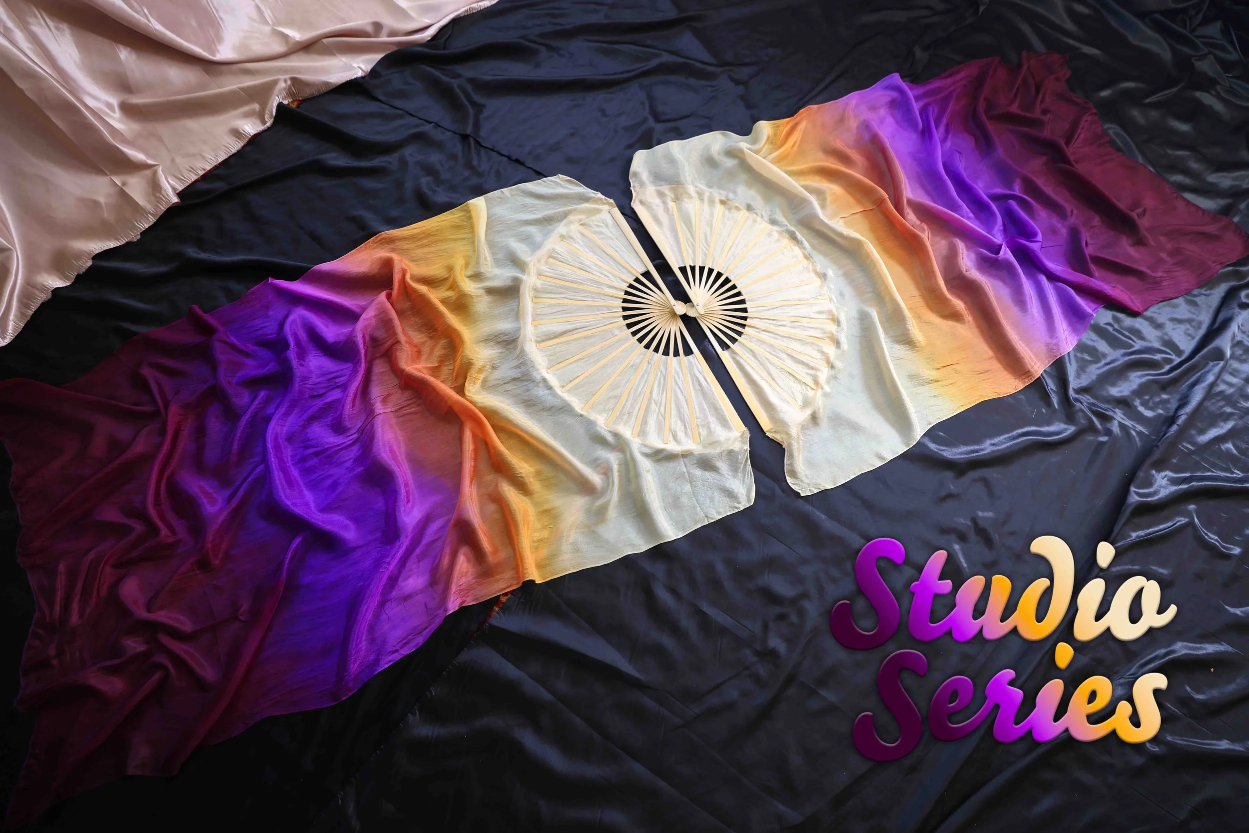 A colorful fabric backdrop with a rainbow gradient, a paper fan, and the partially visible words 'studio series' in colorful letters.