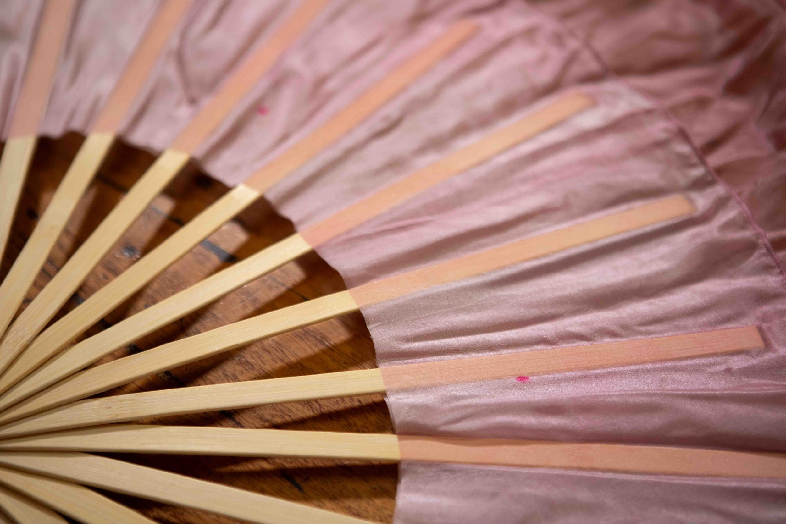 Part of a pink paper fan with wooden spokes on a wooden surface