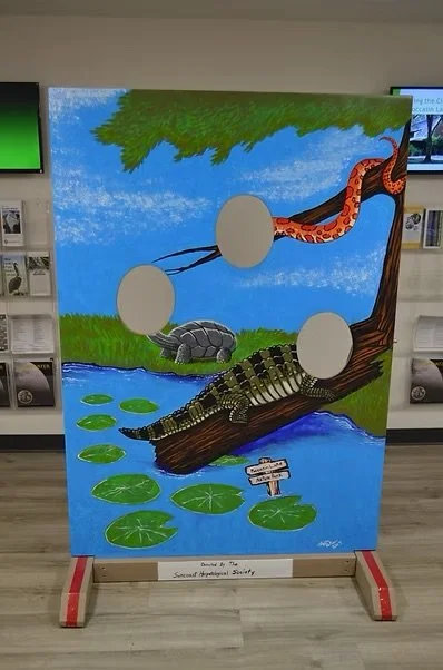 Painting of a nature scene with a snake, a turtle, and a crocodile near water with lily pads and trees.