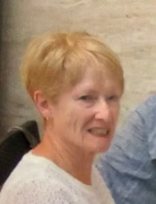 A woman with short, light-colored hair smiling, wearing a light-colored sweater.