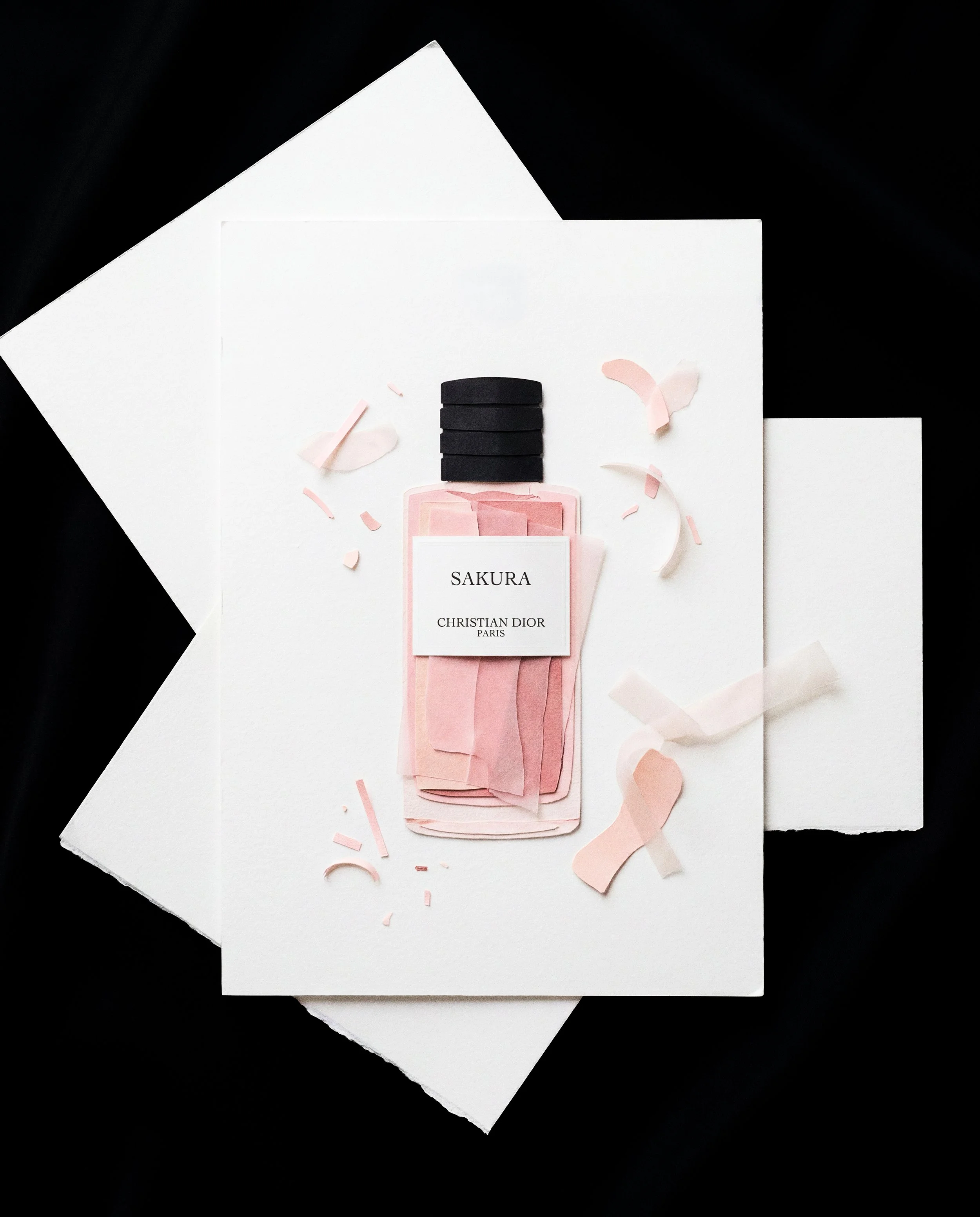 Frascos de perfume en una hoja de papel decorada con papel de seda rosado y confeti, en un fondo negro