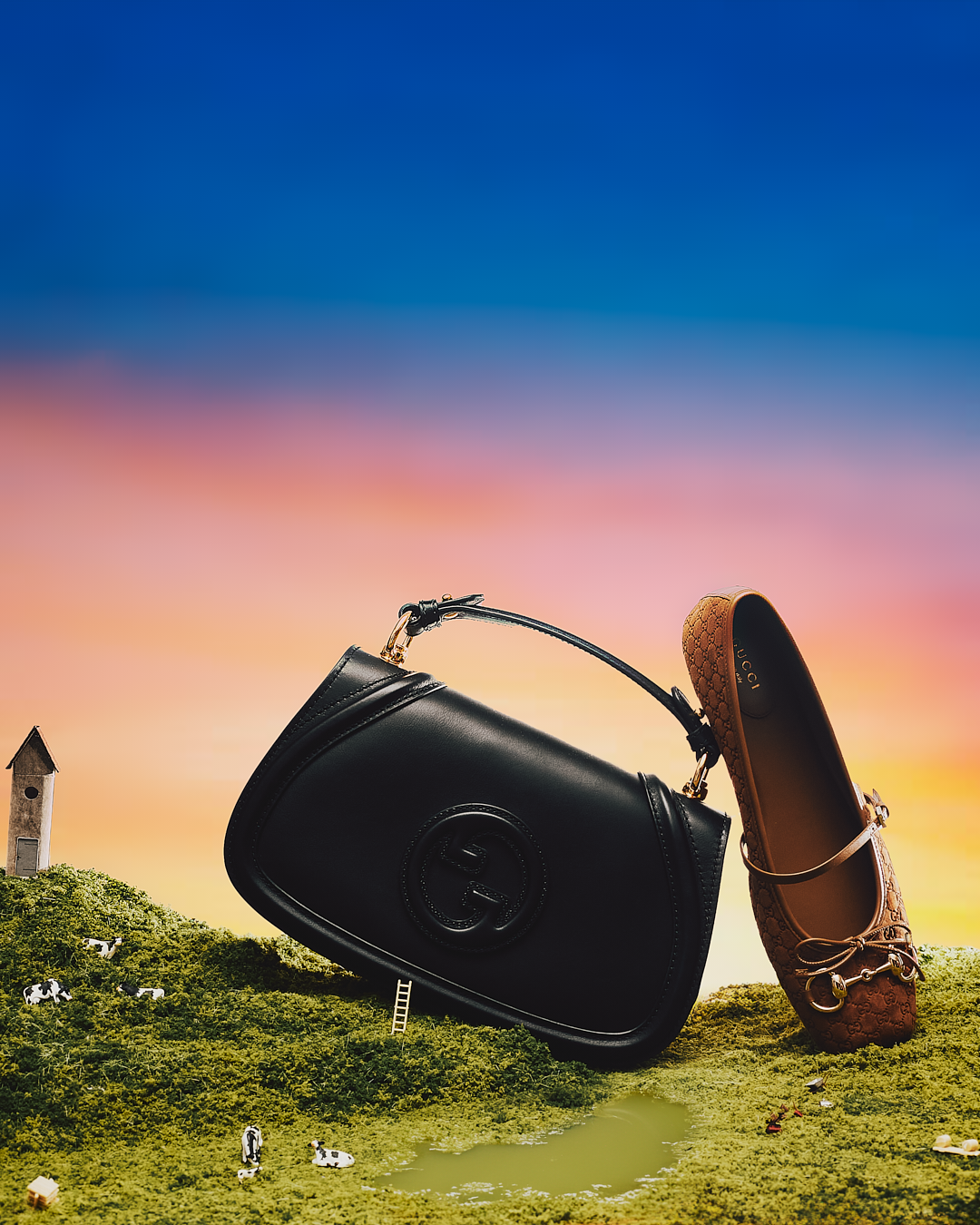 Bolso negro y zapato de diseñador sobre un paisaje con colinas verdes, ciervos y una pequeña torre, con un cielo colorido de atardecer.
