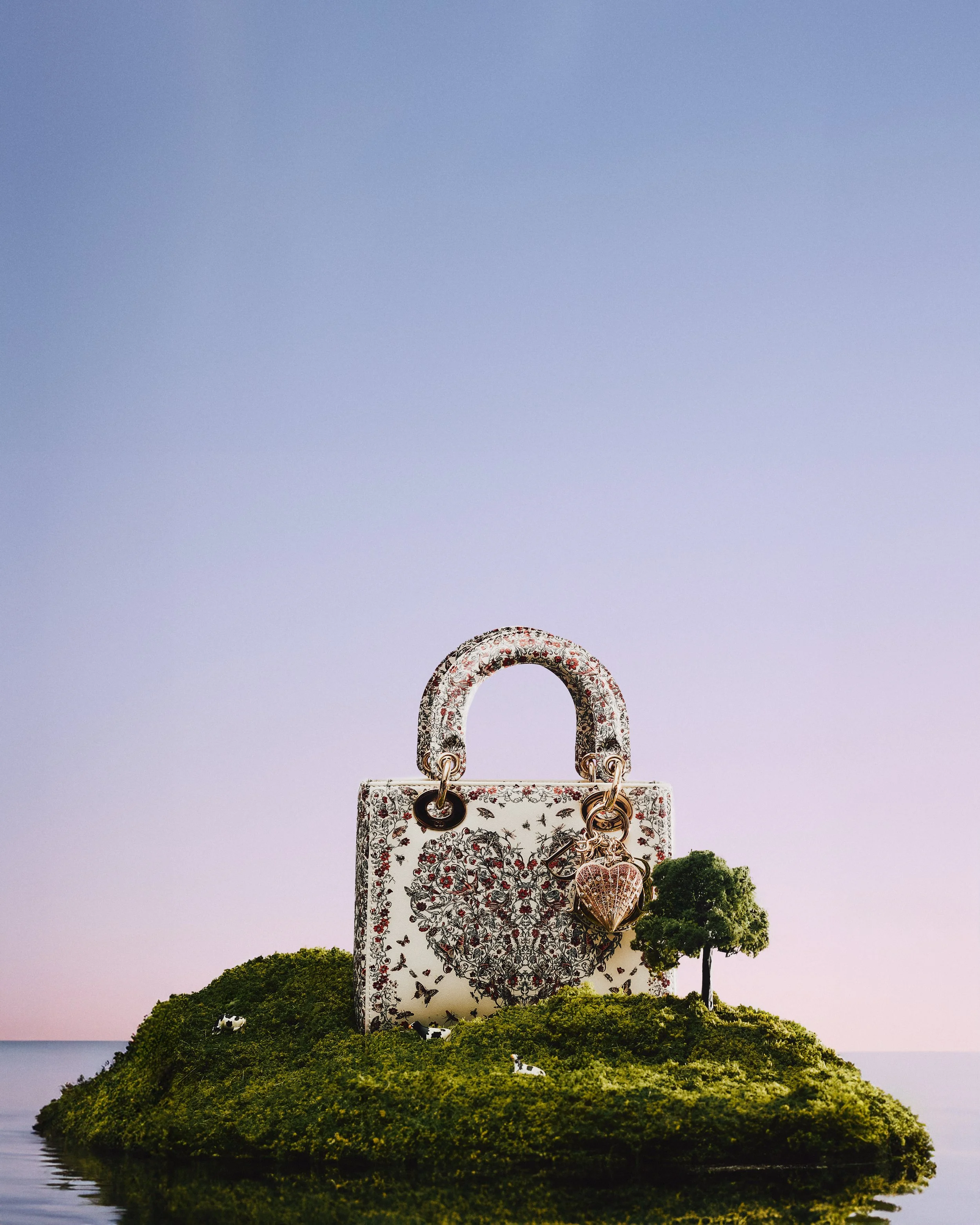 Un bolso decorado con patrones florales y mariposas, rodeado de pequeños árboles y ovejas en una isla, con un cielo claro de fondo.
