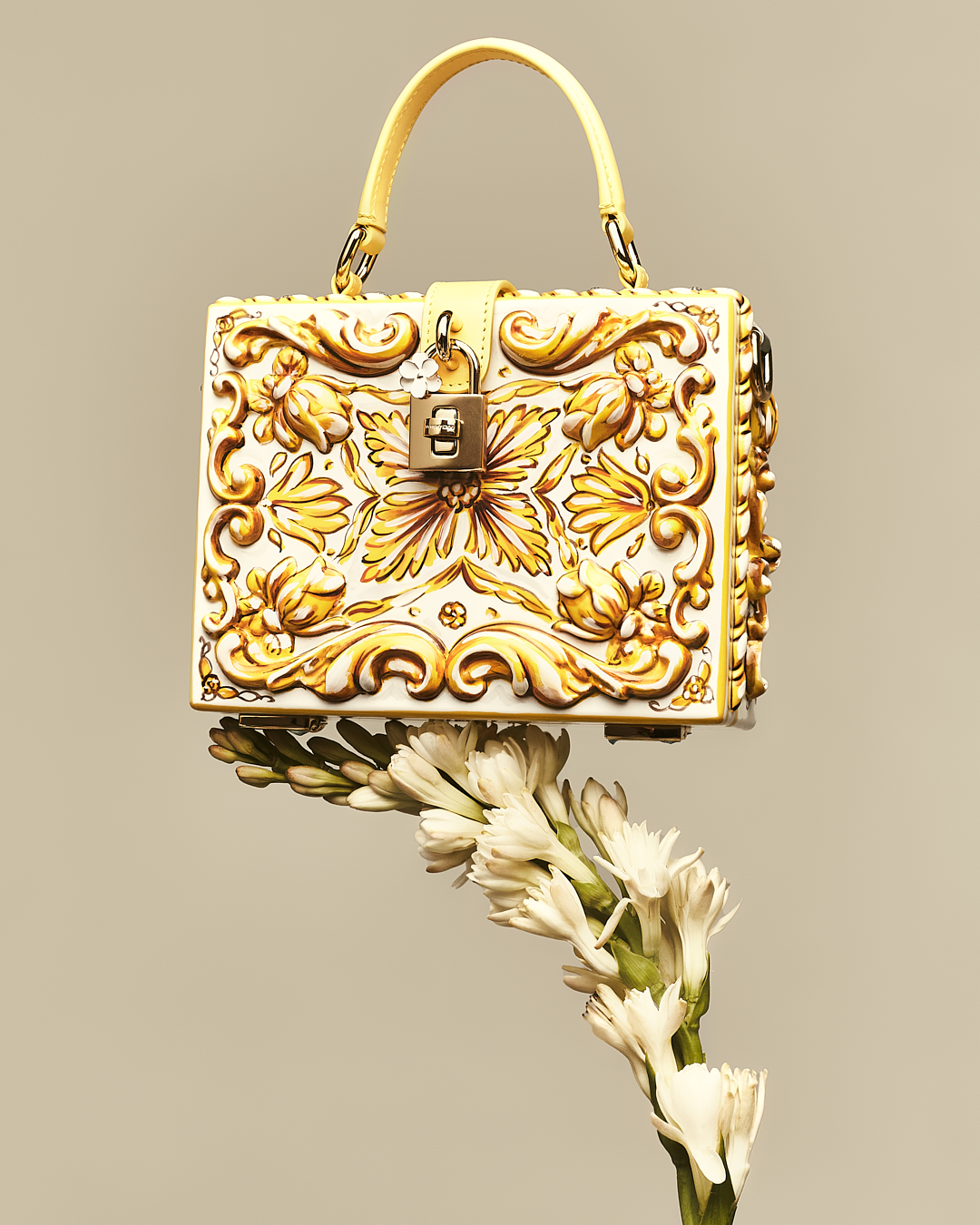 Bolso decorativo de color blanco y dorado con diseño de mariposa y flores, colgado por una correa, con flores blancas debajo.