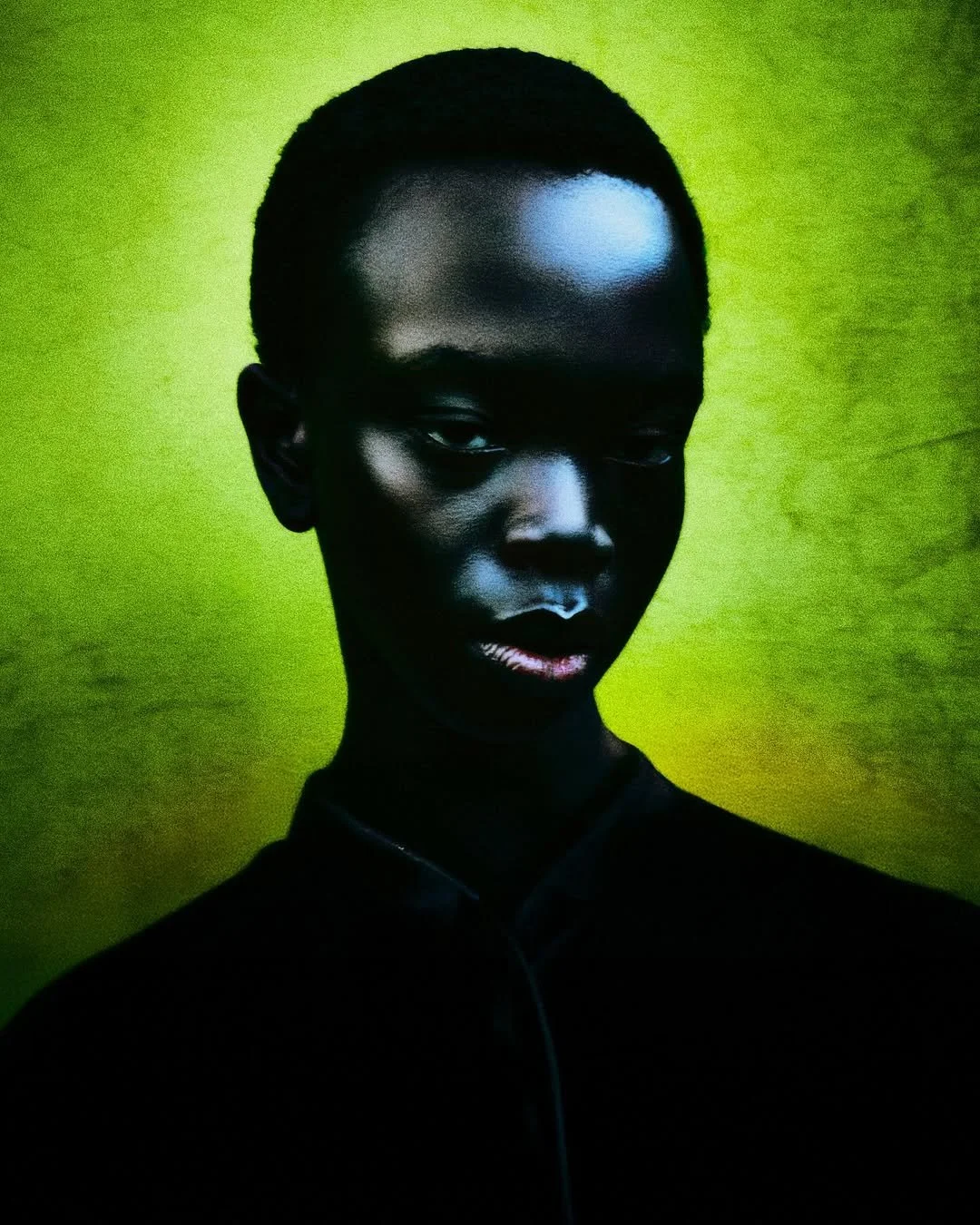 Retrato artístico de una persona joven de piel oscura con cabello corto, fondo verde brillante, expresión seria y mirada fija.